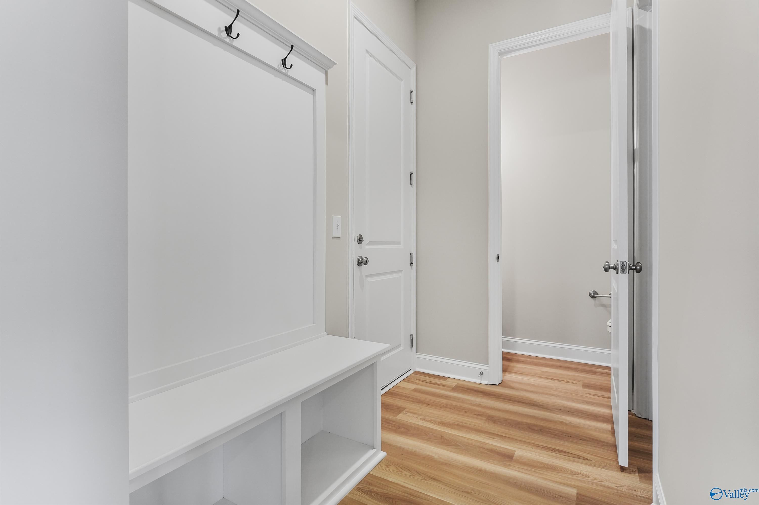 White mudroom with built-in bench, coat hooks, and storage cubbies on oak floors in Evermore Homes The Haven, Owens Cross Roads, AL