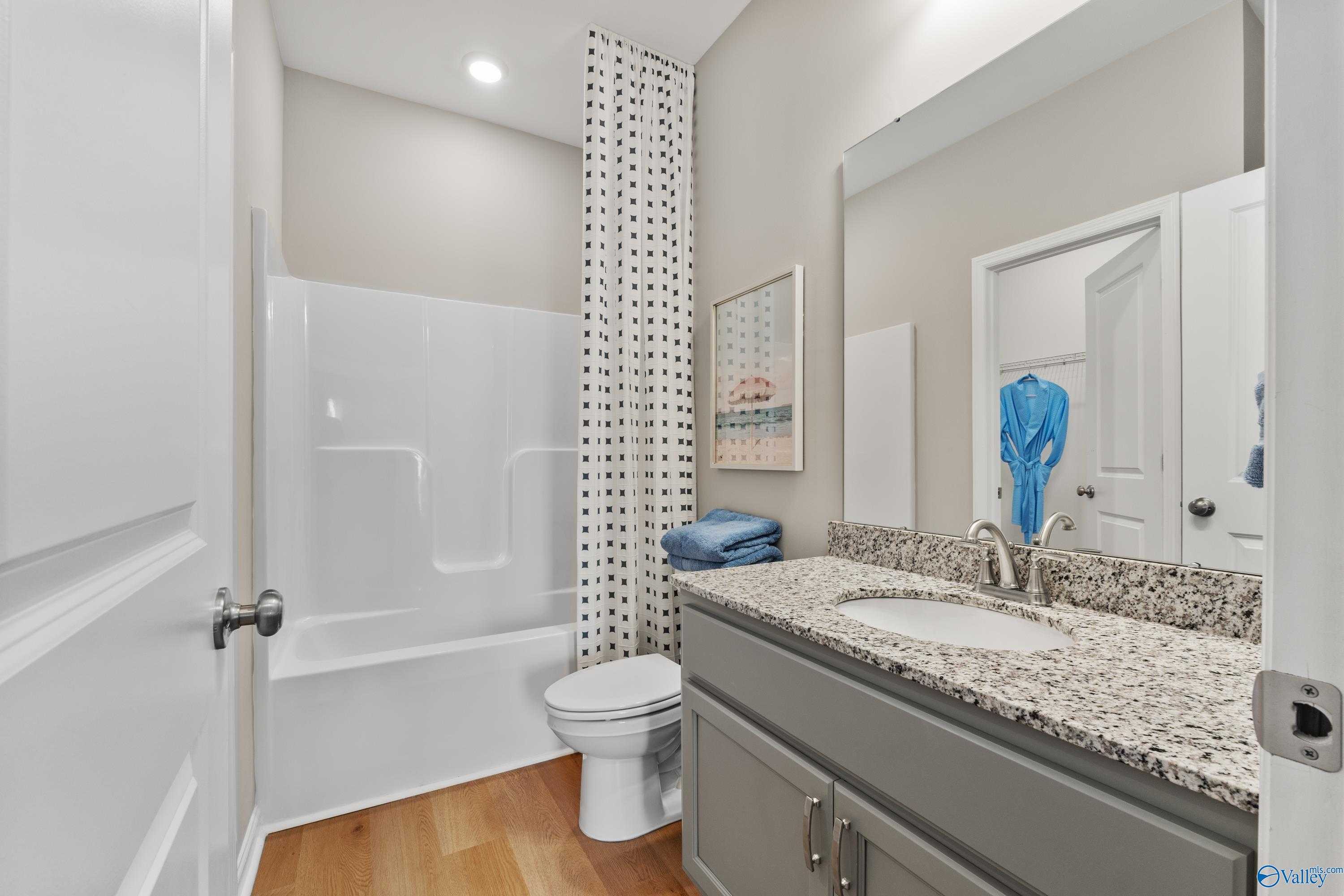 Modern bathroom with granite vanity, white tub-shower combo, and blue accents in 4-bedroom Davidson Homes The Sanctuary, Athens, Alabama
