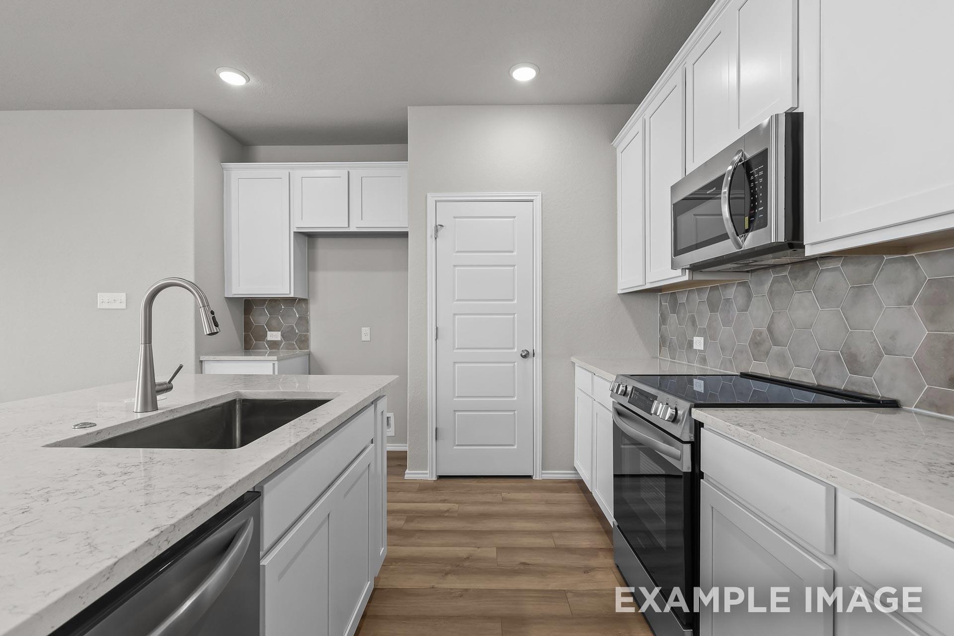 Modern kitchen with white cabinets, quartz countertops, and hexagon backsplash in The Colorado G home in Heartland, Texas.