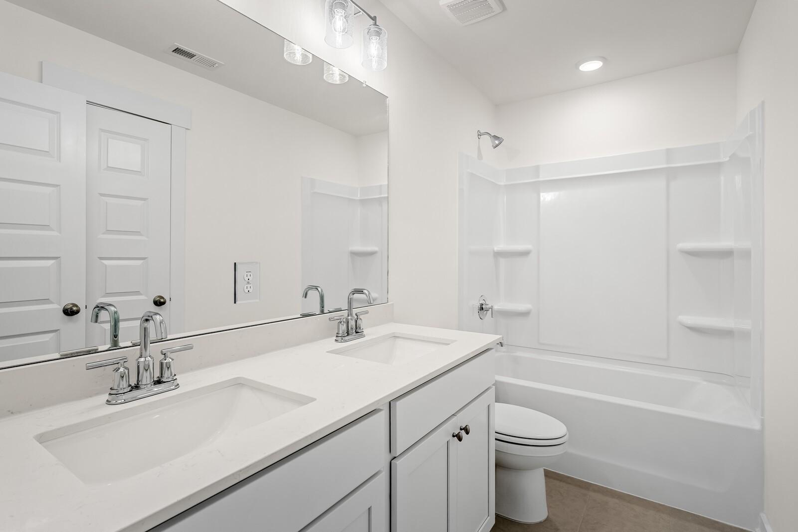 Modern bathroom with double vanity, white cabinets, and shower-tub combo in The Ridgeport D at Benders Cove, Mt. Juliet.