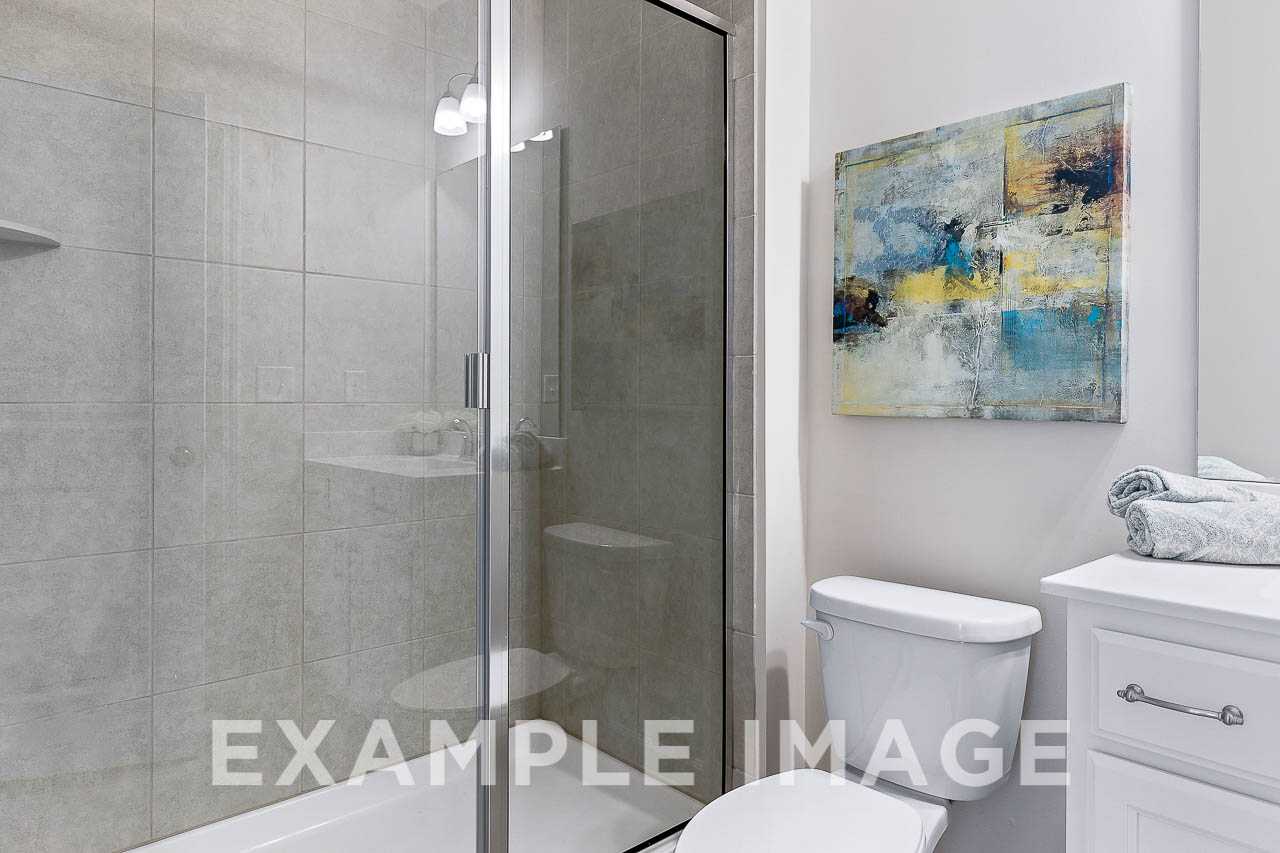 Modern master bathroom in The Willow C featuring frameless glass shower, white vanity, toilet, and abstract wall art