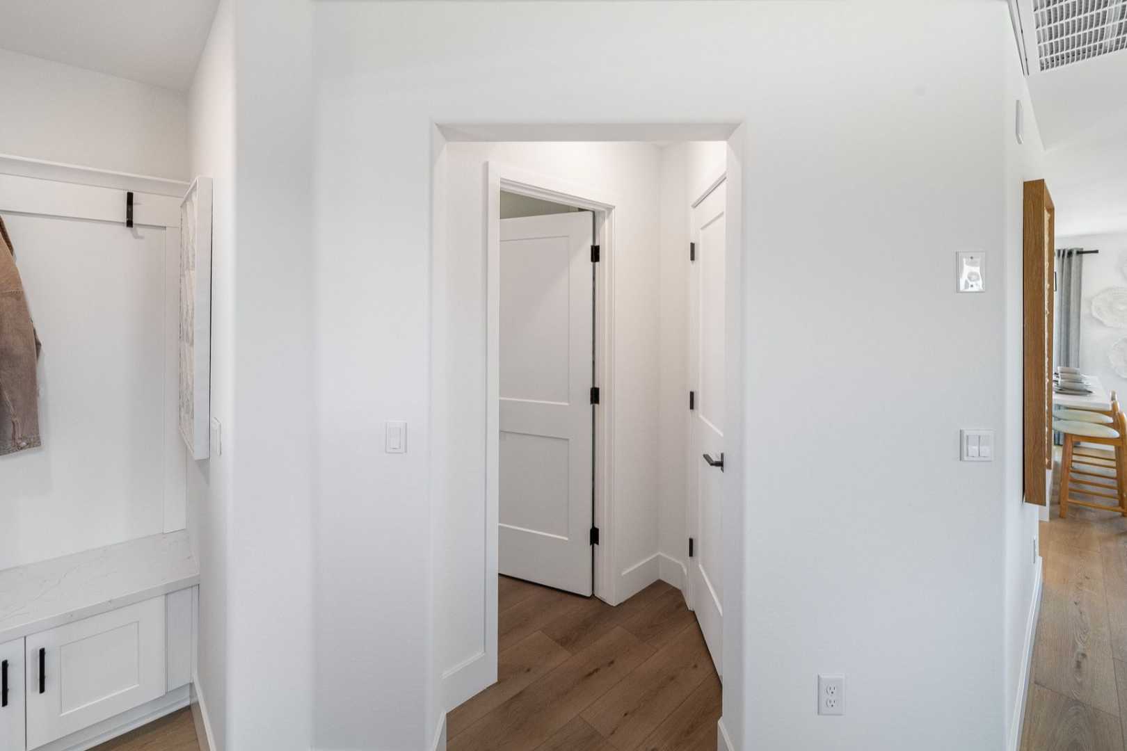 Modern mudroom in The Wilmington showcasing white walls, coat hooks with jacket, built-in bench, and adjacent dining area