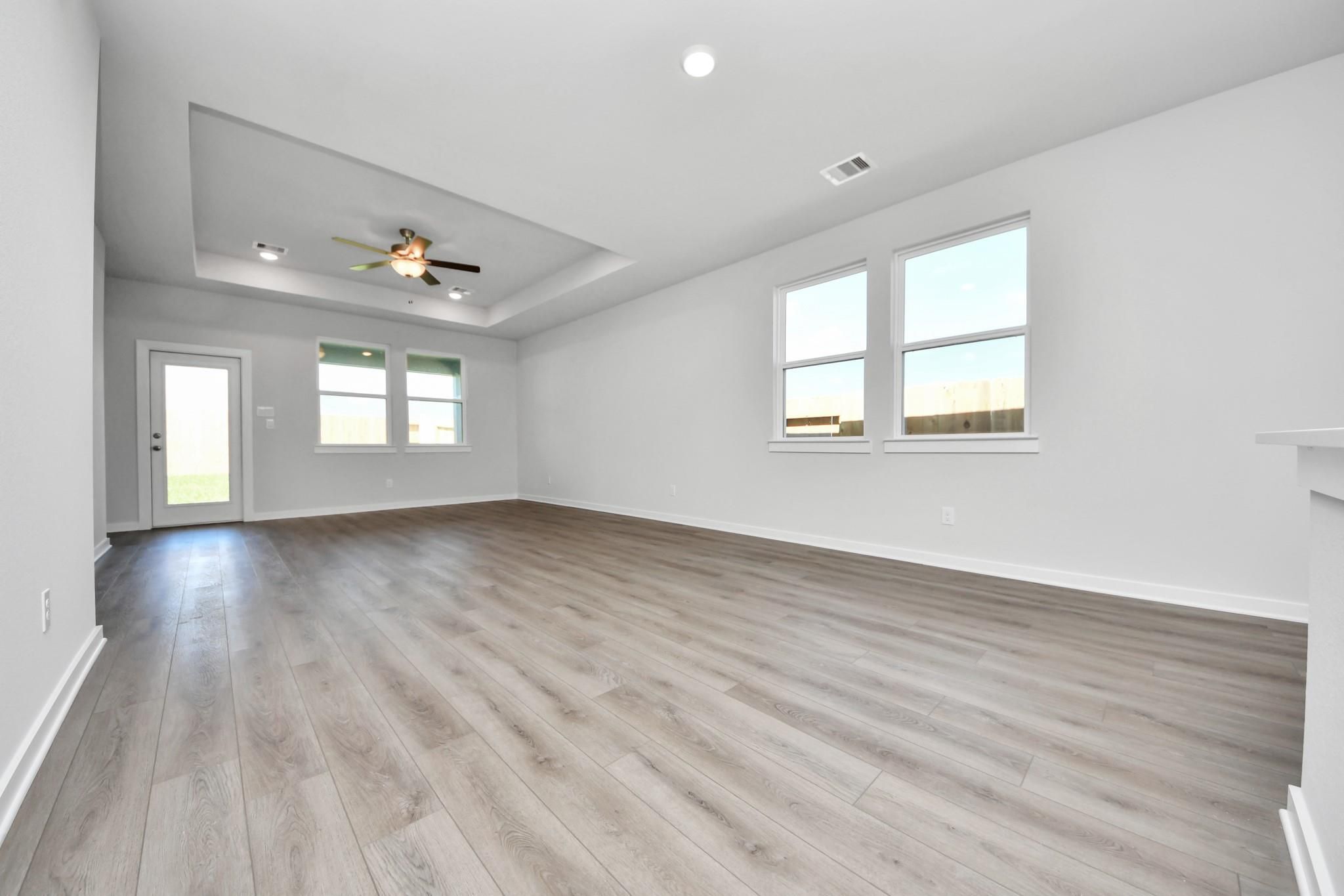 Spacious living room with tray ceiling and wood-style flooring in The Riviera A floor plan at Emberly in Beasley, Texas.