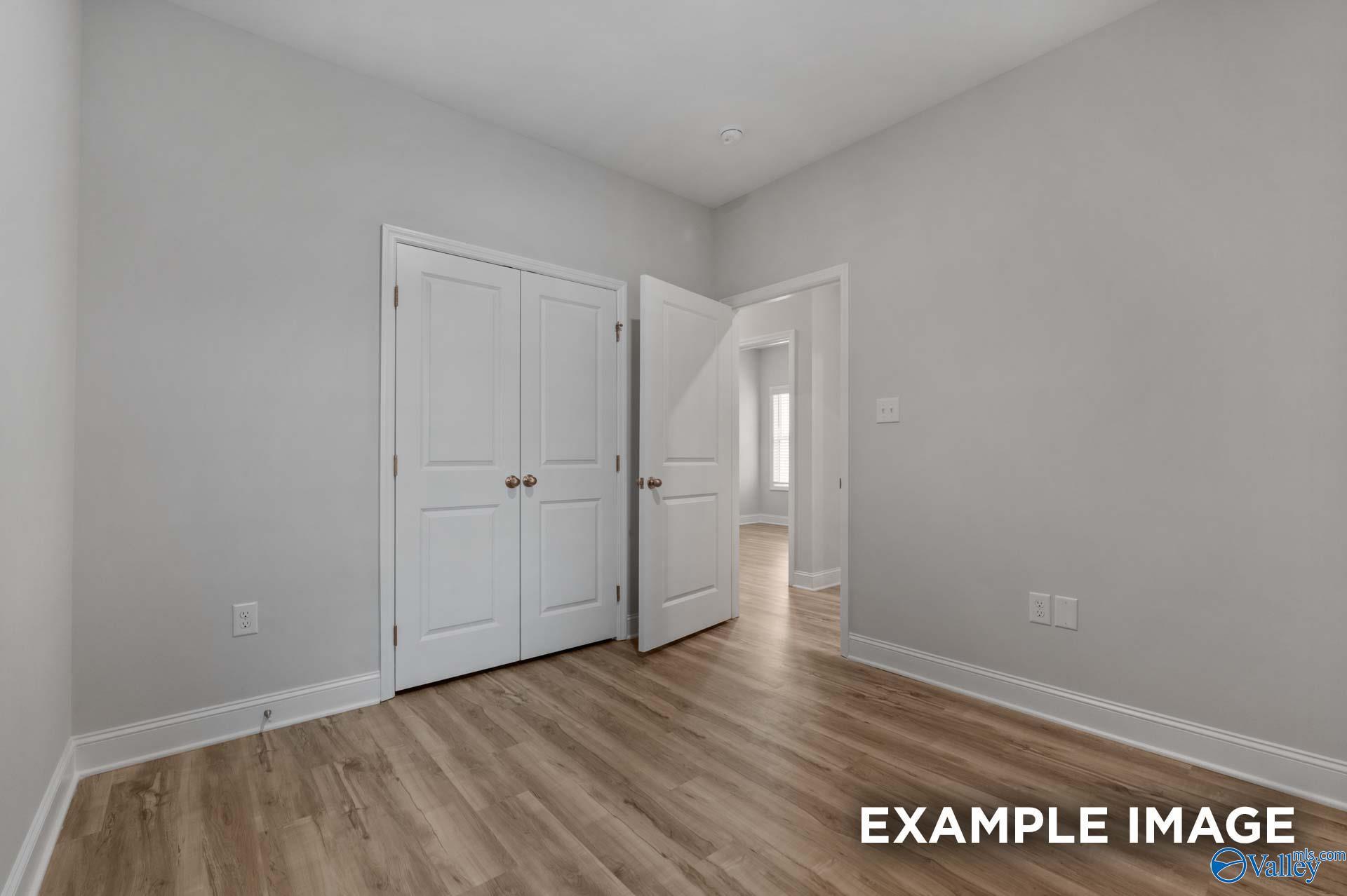 Spacious secondary bedroom with double closet doors, light gray walls, and hardwood floors in Davidson Homes The Cumberland B, Decatur, Alabama
