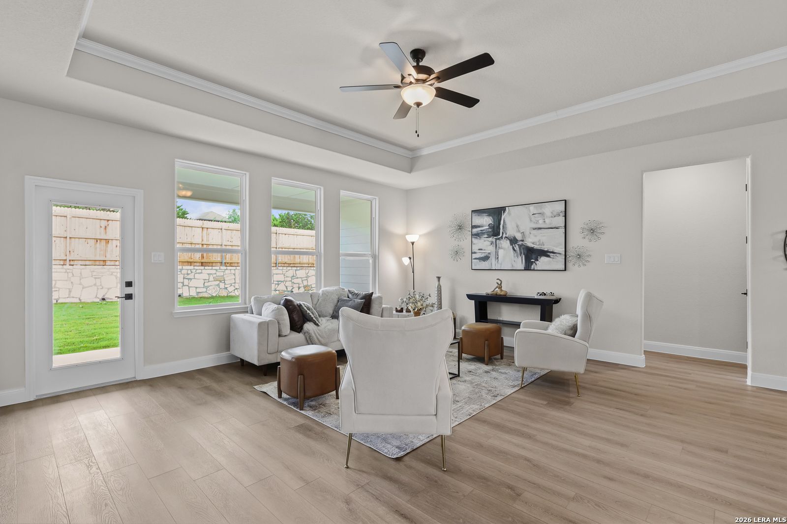 Bright living room with white sofa, accent chairs, ceiling fan, and backyard views in Davidson Homes The Lanier G, Castroville, Texas