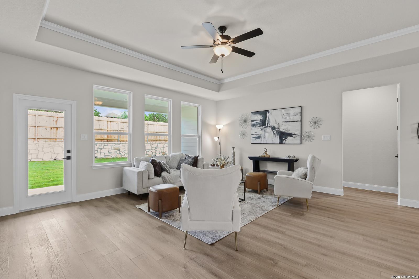 Bright living room with white sofa, accent chairs, ceiling fan, and backyard views in Davidson Homes The Lanier G, Castroville, Texas