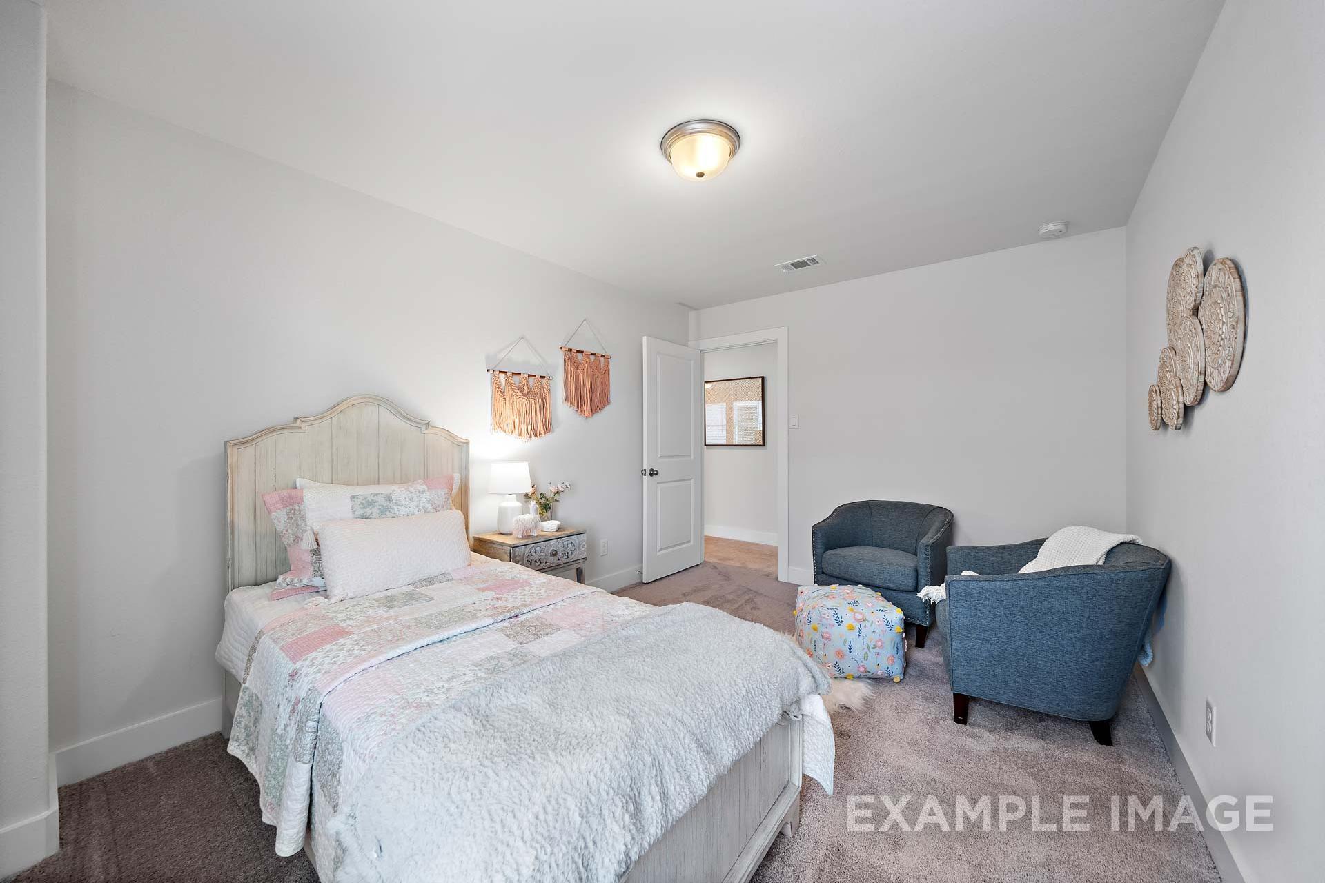 Cozy secondary bedroom in The Rose B Davidson Homes plan with tufted bed, blue armchairs, woven wall hangings