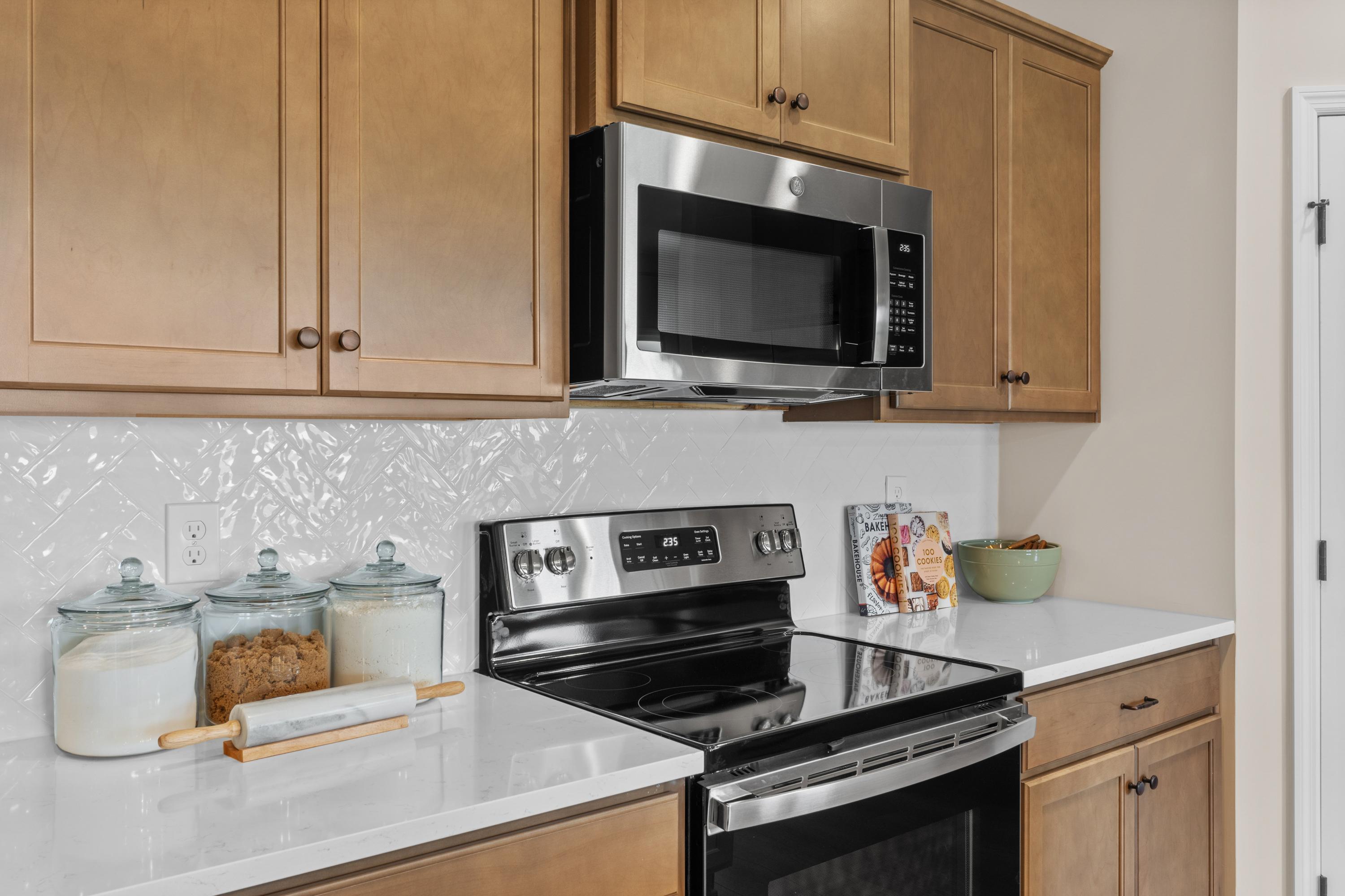 Spacious kitchen in The Daphne F with oak shaker cabinets, stainless steel microwave and range, white subway tile backsplash