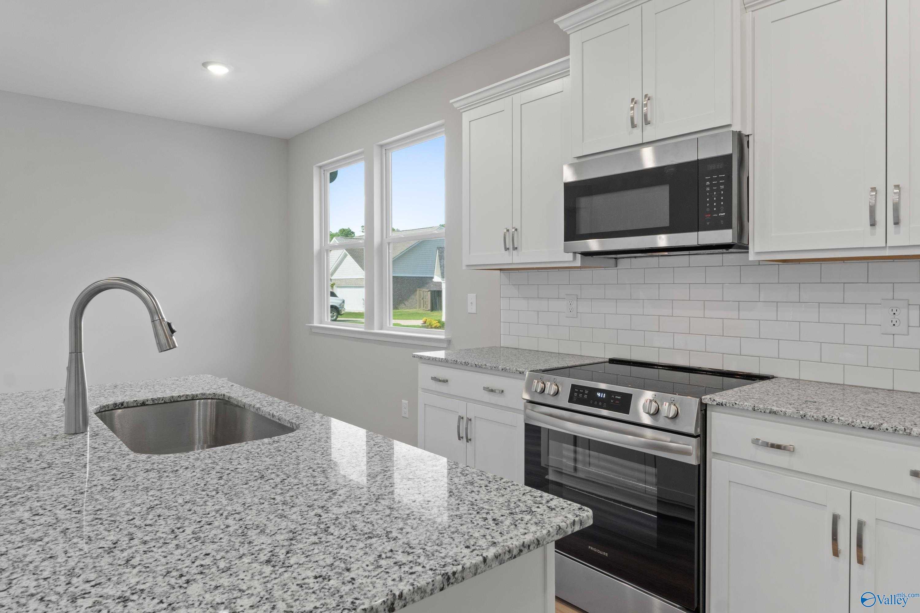 Modern kitchen with granite island, stainless appliances, white cabinets, and subway tile backsplash in The Polaris 3-bedroom home, Fayetteville TN