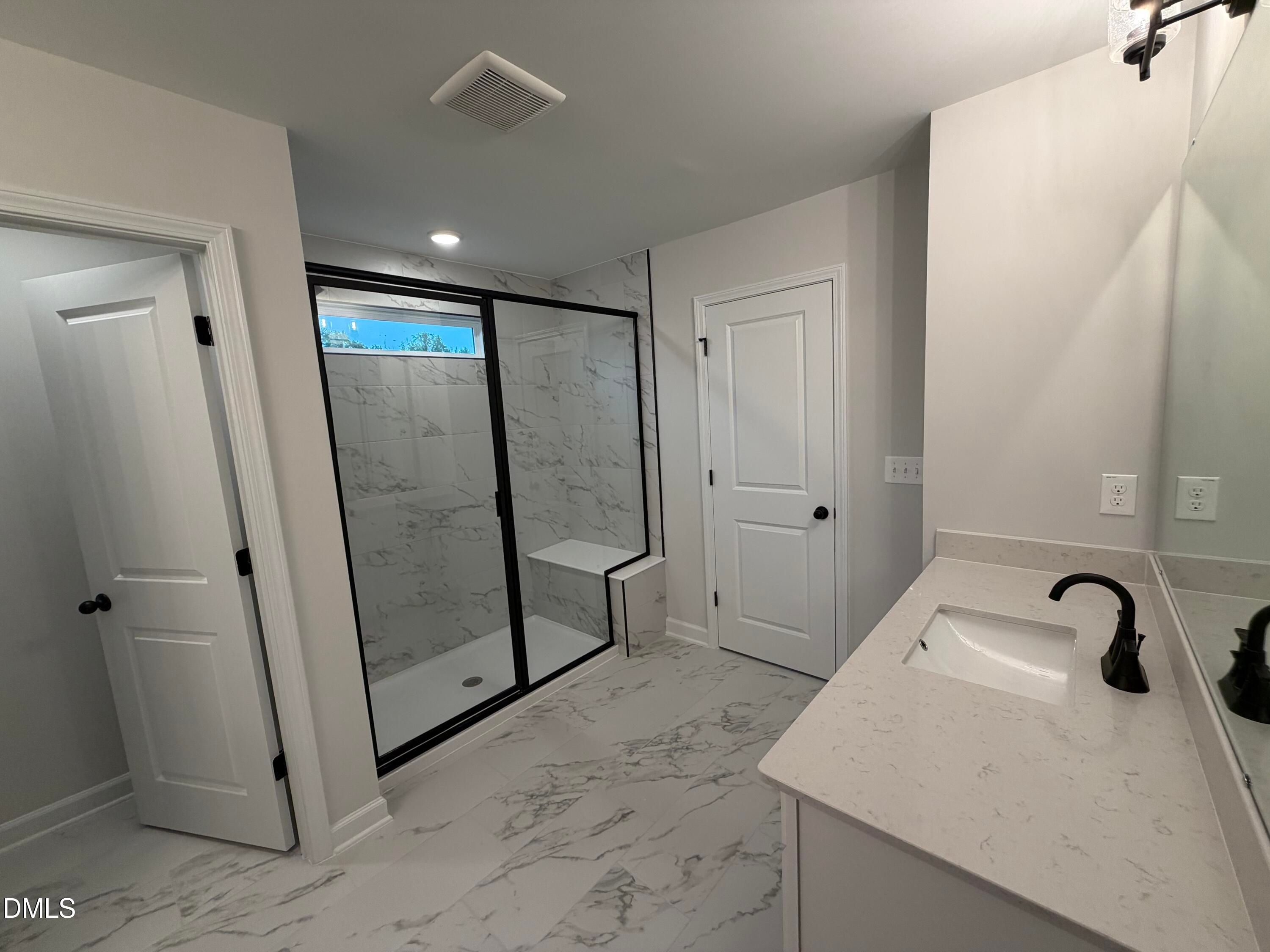 Modern primary bathroom with marble tile walk-in shower, matte black fixtures, and quartz vanity in Davidson Homes Preston C, Wendell NC
