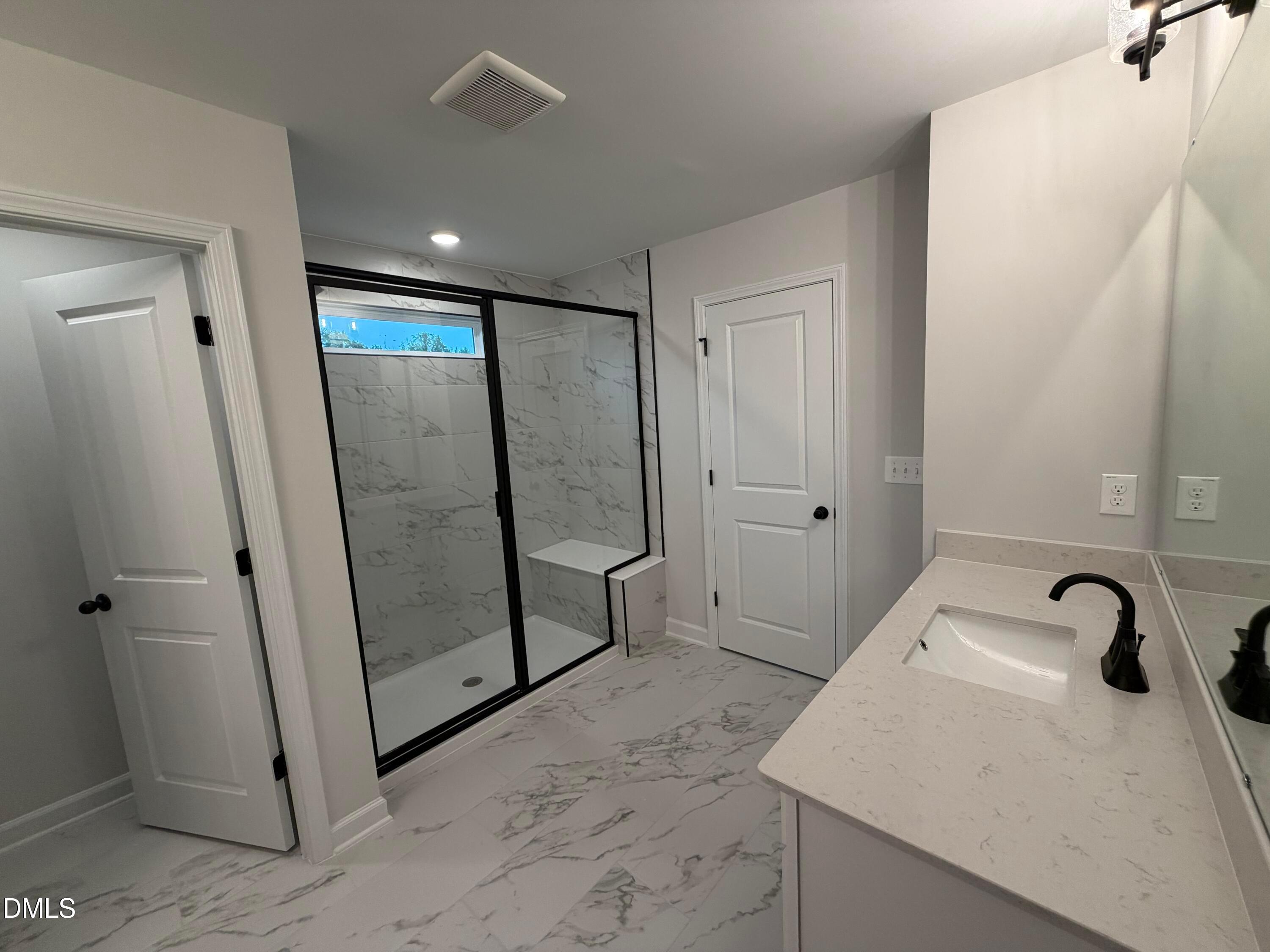Modern primary bathroom with marble tile walk-in shower, matte black fixtures, and quartz vanity in Davidson Homes Preston C, Wendell NC