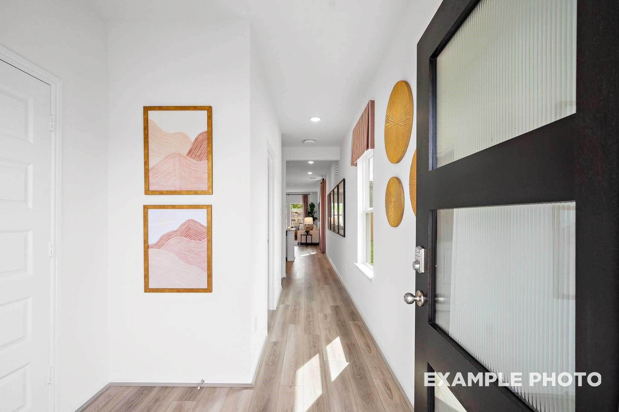 Bright hallway with pink mountain artwork, rattan wall decor, and frosted glass door in Davidson Homes Sabine F, Magnolia Texas