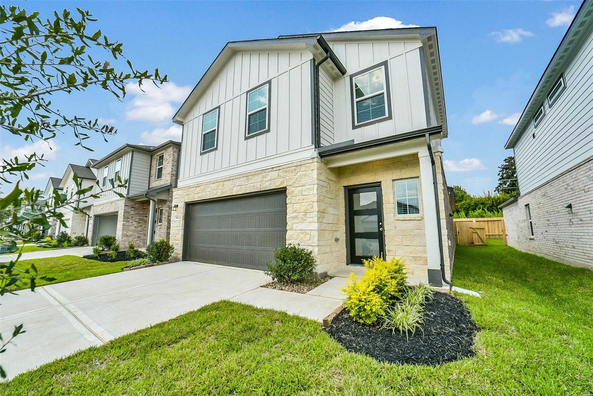 Two-story Blanco E home by Davidson Homes with white shiplap siding, stone accents, two-car garage, and landscaped yard in Lakes at Black Oak, Magnolia, Texas