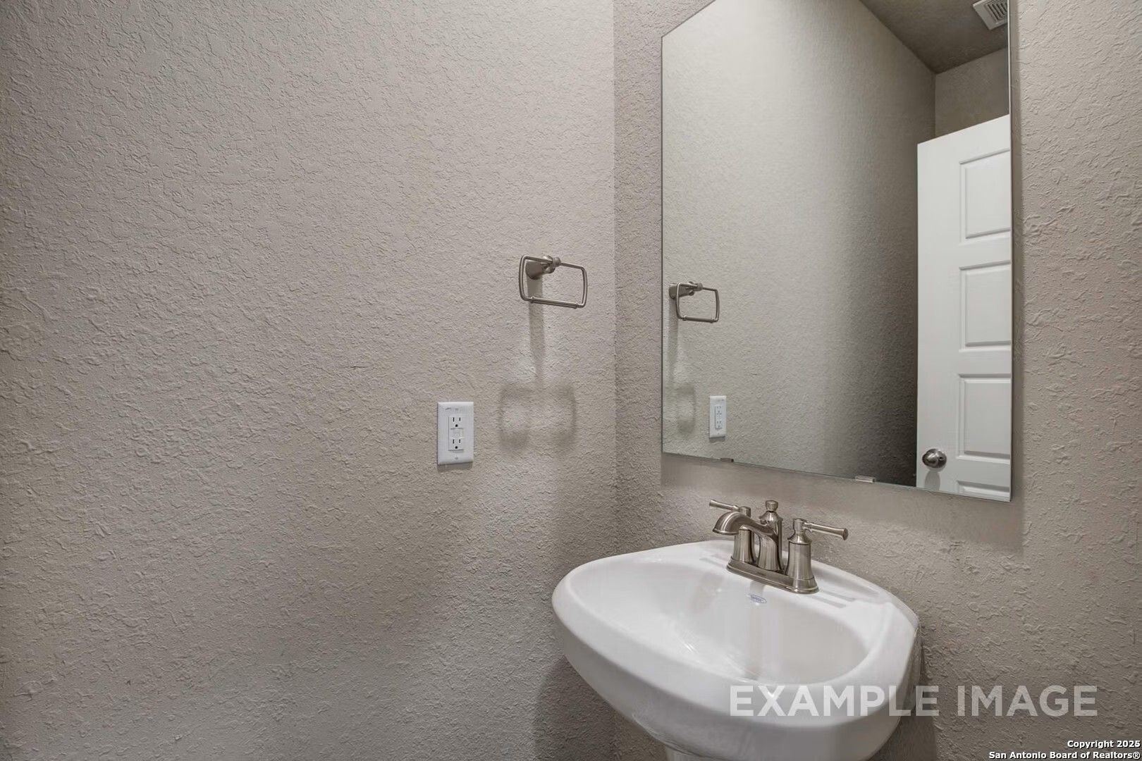 Modern powder room featuring white pedestal sink, chrome faucet, and frameless mirror in Davidson Homes The Murray K, San Antonio, Texas