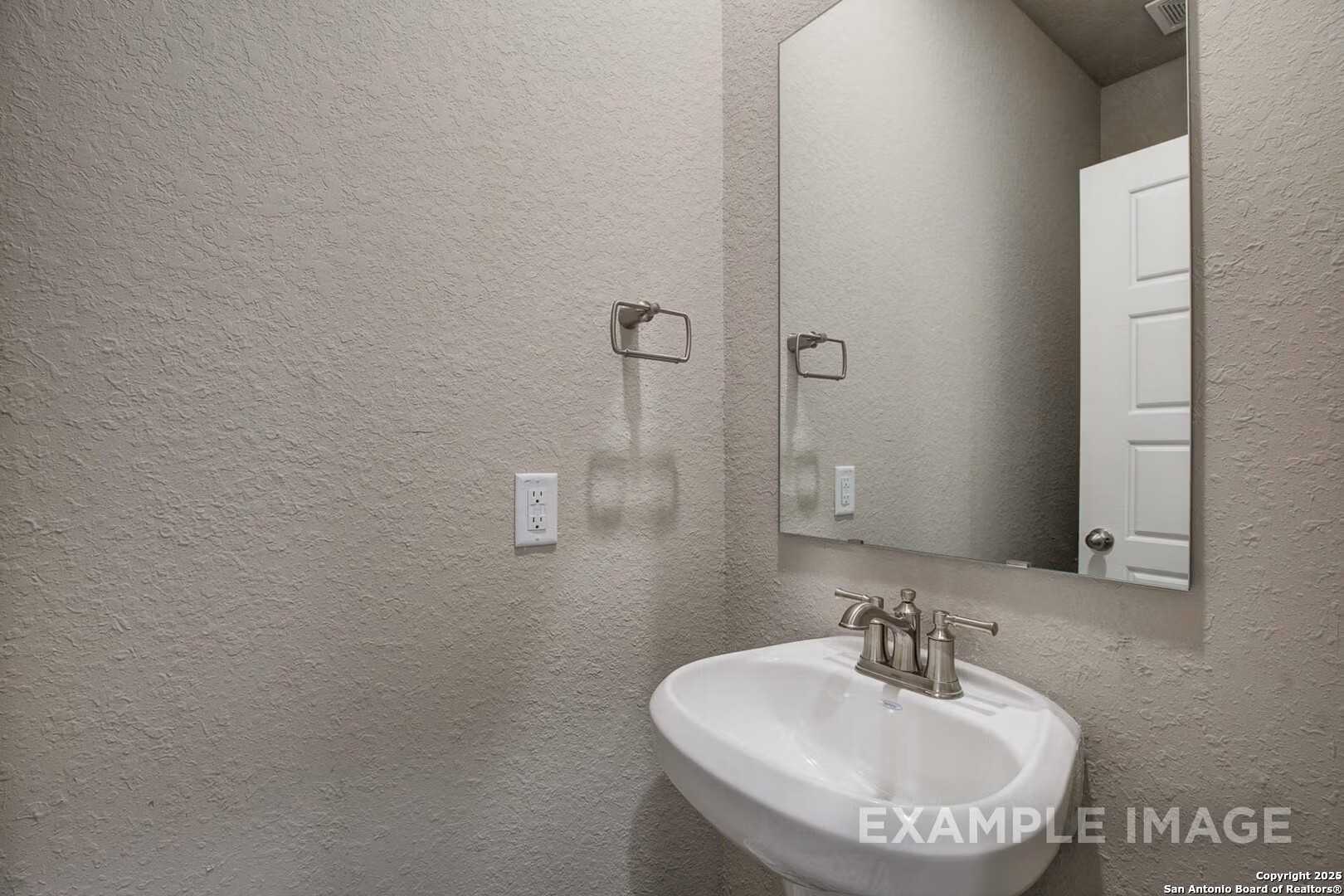 Modern powder room featuring white pedestal sink, chrome faucet, and frameless mirror in Davidson Homes The Murray K, San Antonio, Texas