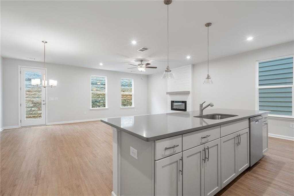 Modern open-concept kitchen with gray island, white cabinets, and adjacent living room featuring fireplace in The Cary A, Kennesaw, GA