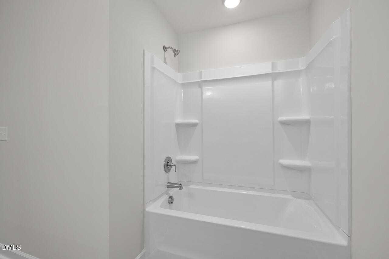 Modern white shower-tub combo with built-in shelves and glass door in Davidson Homes The Warren bathroom, Fuquay-Varina, NC