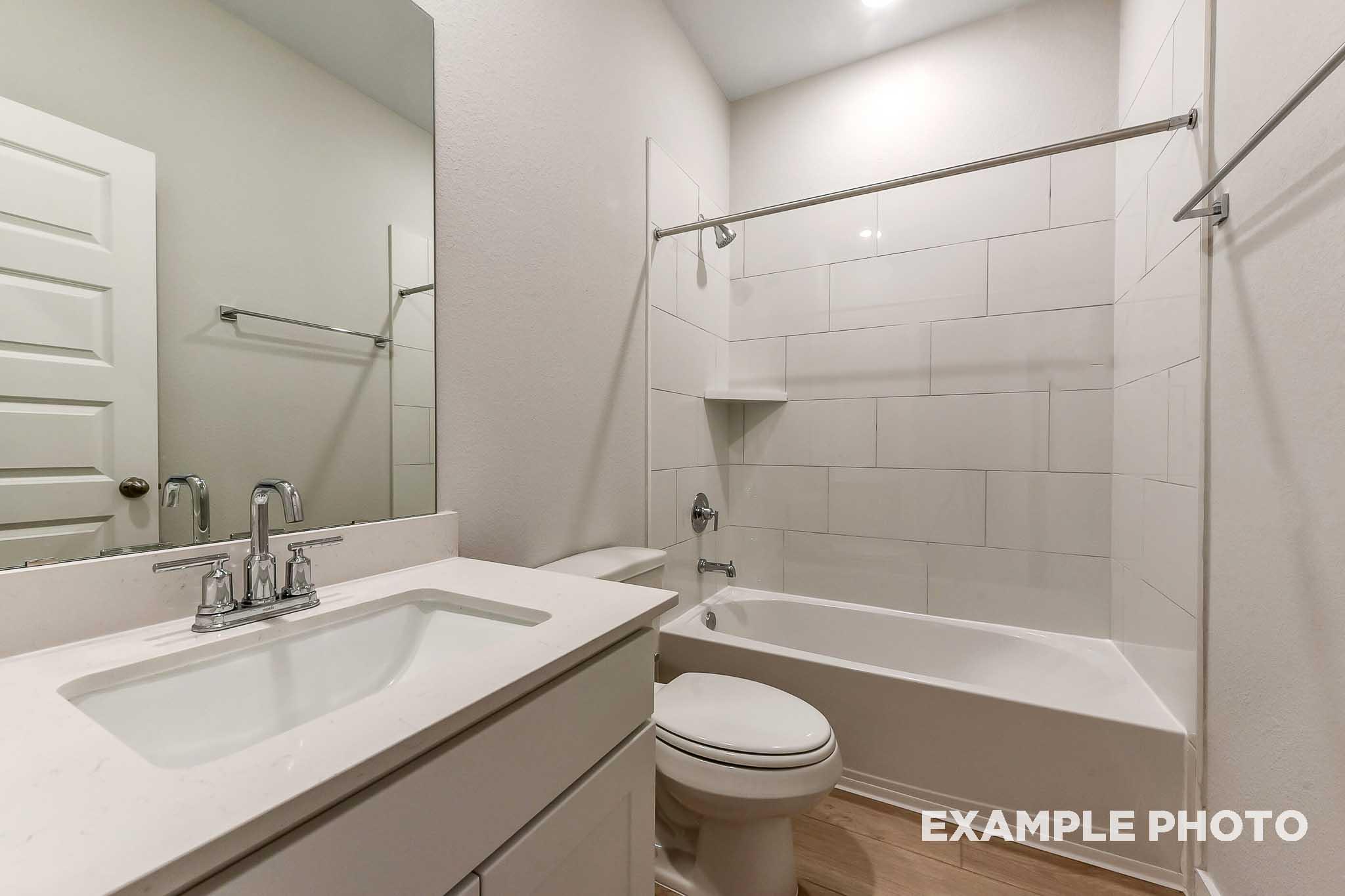 Modern bathroom in The Laguna B with white subway tile tub-shower, single vanity sink, large mirror, and toilet by Davidson Homes