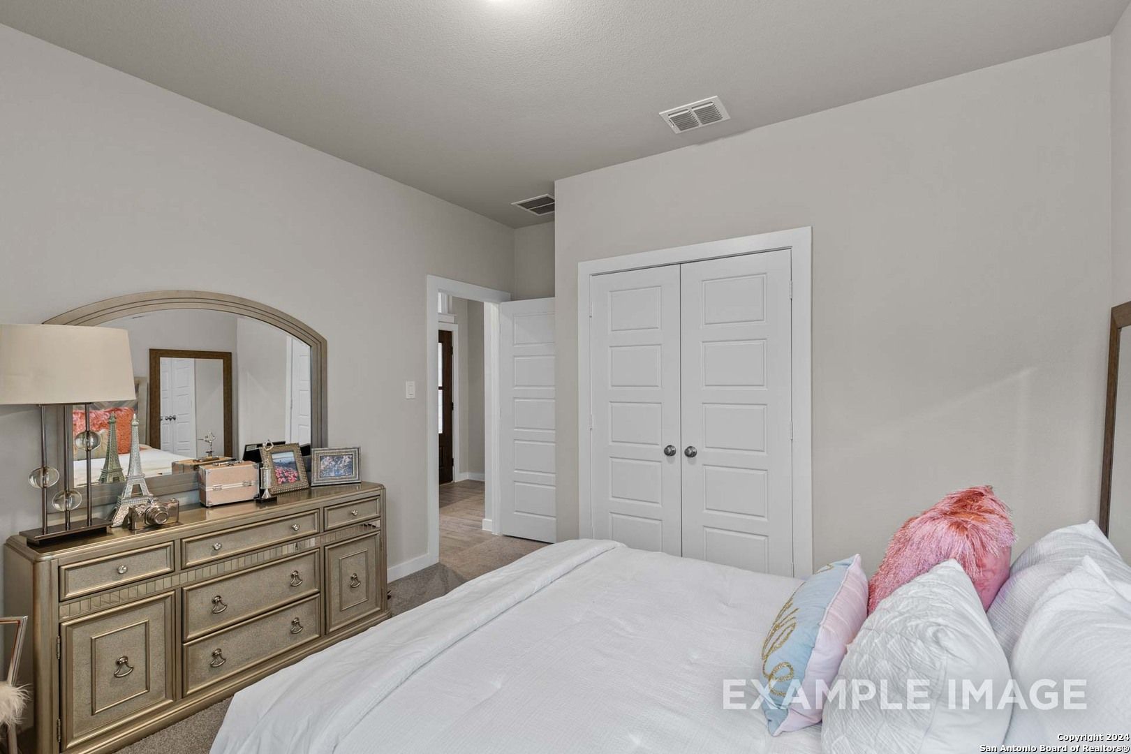 Cozy secondary bedroom with wooden dresser, mirrored vanity, and plush bed in Davidson Homes The Collin A, Hannah Heights, Seguin, Texas