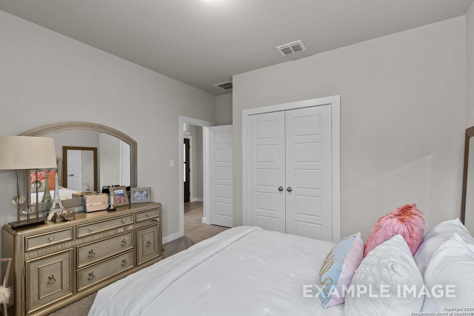 Cozy secondary bedroom with wooden dresser, mirrored vanity, and plush bed in Davidson Homes The Collin A, Hannah Heights, Seguin, Texas