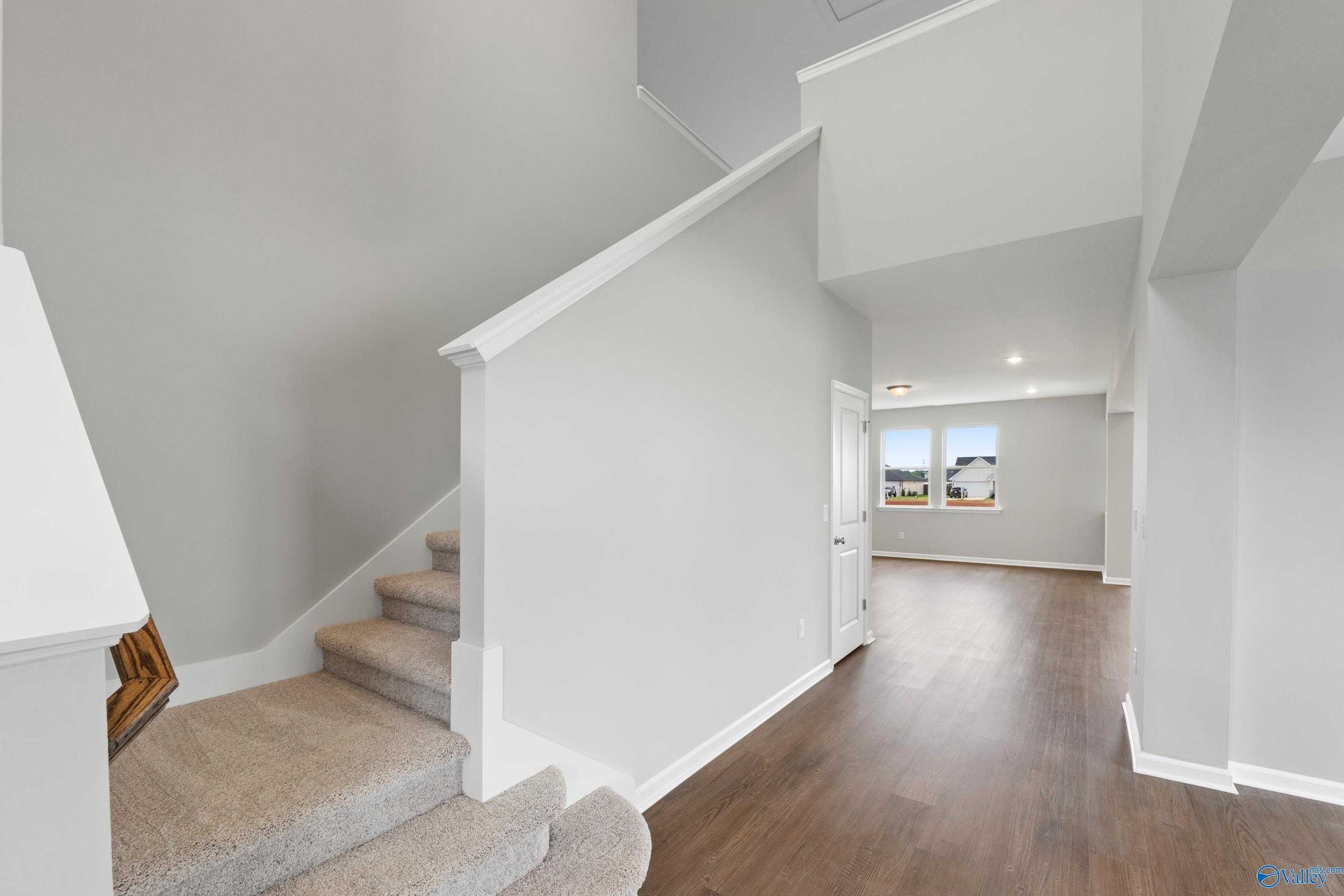 Elegant curved staircase with beige carpet and hardwood hallway in 2-story The Dorado home, Davidson Homes, Athens Alabama