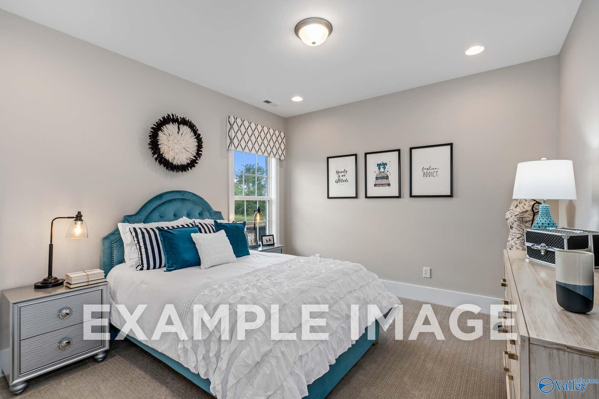 Teal upholstered bed with white ruffled bedding in bright bedroom of Davidson Homes The Harrison plan in Hartselle, Alabama