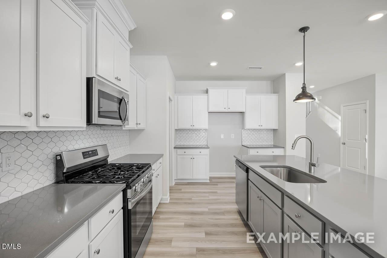 Modern kitchen with white shaker cabinets, stainless steel gas range, quartz island sink, hexagon tile backsplash in Adalynn B, Lillington NC