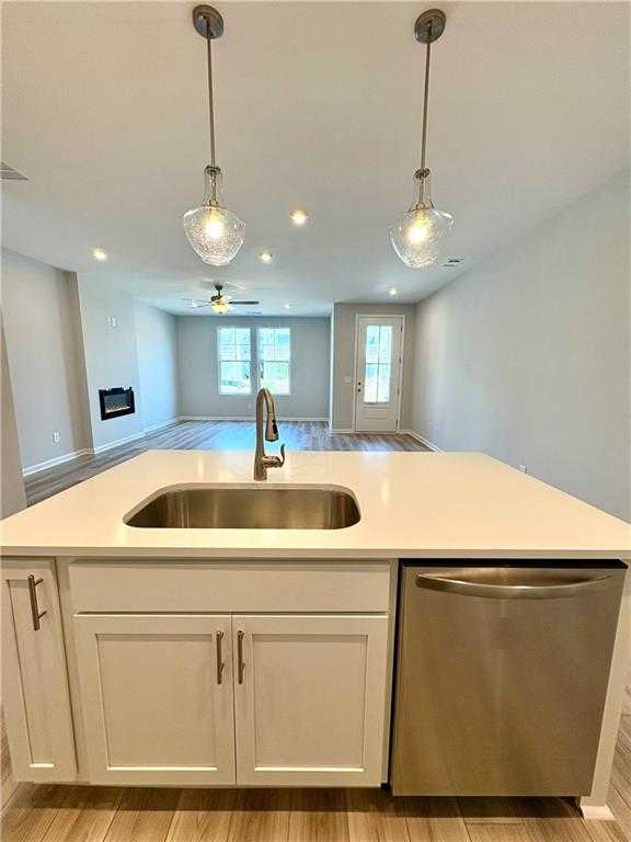 Modern kitchen island with stainless steel sink, dishwasher, and pendant lights in open-concept The Monroe A home, Emerson, Georgia
