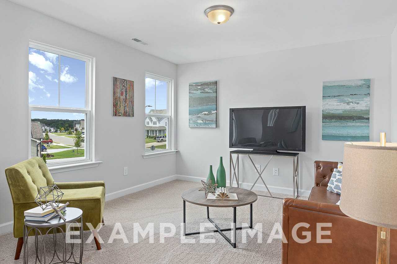 Spacious living room in The Willow C featuring large windows with neighborhood view, green armchairs, leather sofa, and abstract art