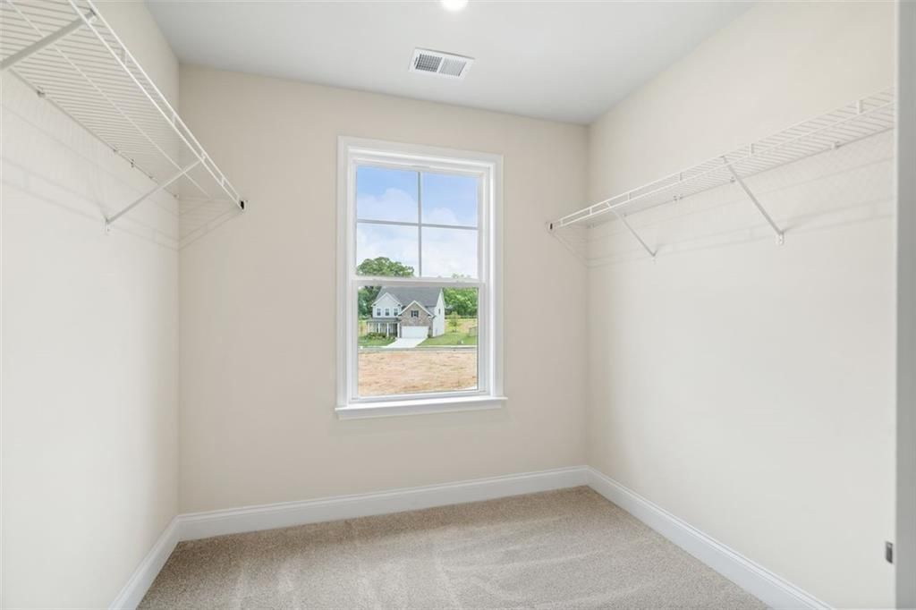 Spacious walk-in closet with wire shelving, hanging rods, and window view in Davidson Homes The Willow B, Hoschton, Georgia