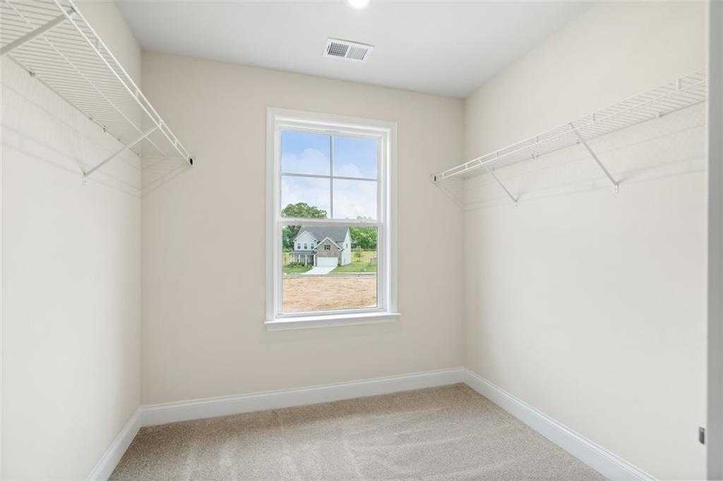 Spacious walk-in closet with wire shelving, hanging rods, and window view in Davidson Homes The Willow B, Hoschton, Georgia