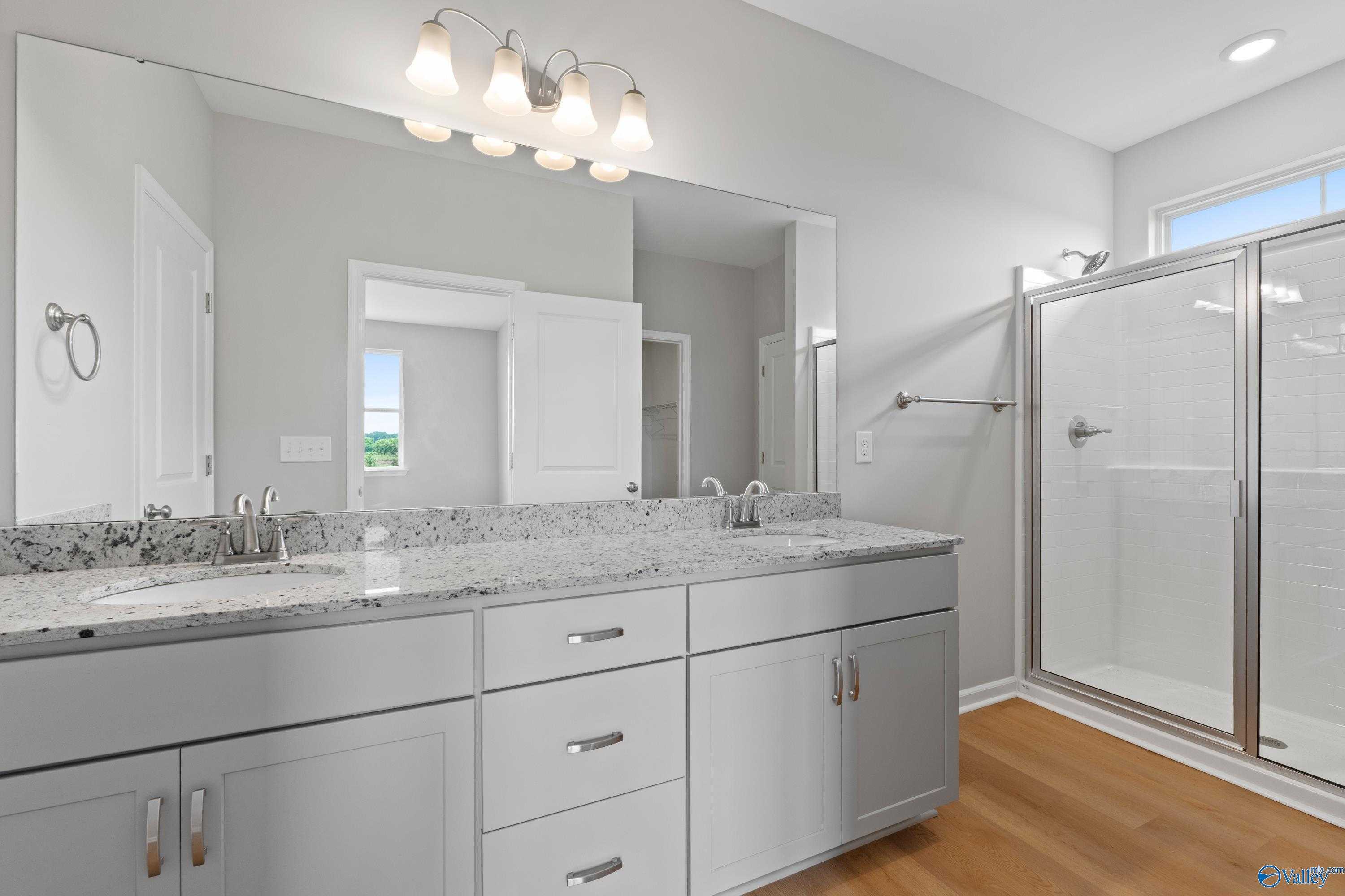 Modern master bathroom featuring double granite vanity, frameless glass shower, and gray cabinetry in Davidson Homes The Orion, Athens AL