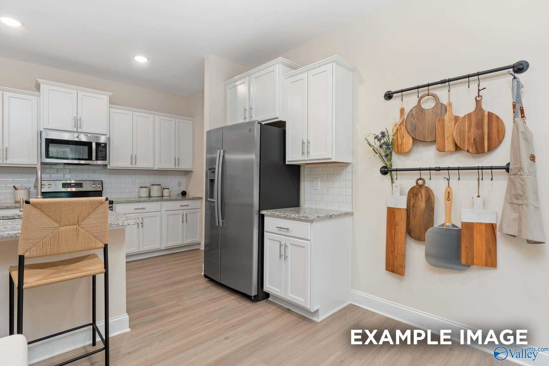 Modern kitchen with white shaker cabinets, stainless steel fridge, subway tile backsplash, and hanging utensils in The Camden B by Davidson Homes, Huntsville, AL