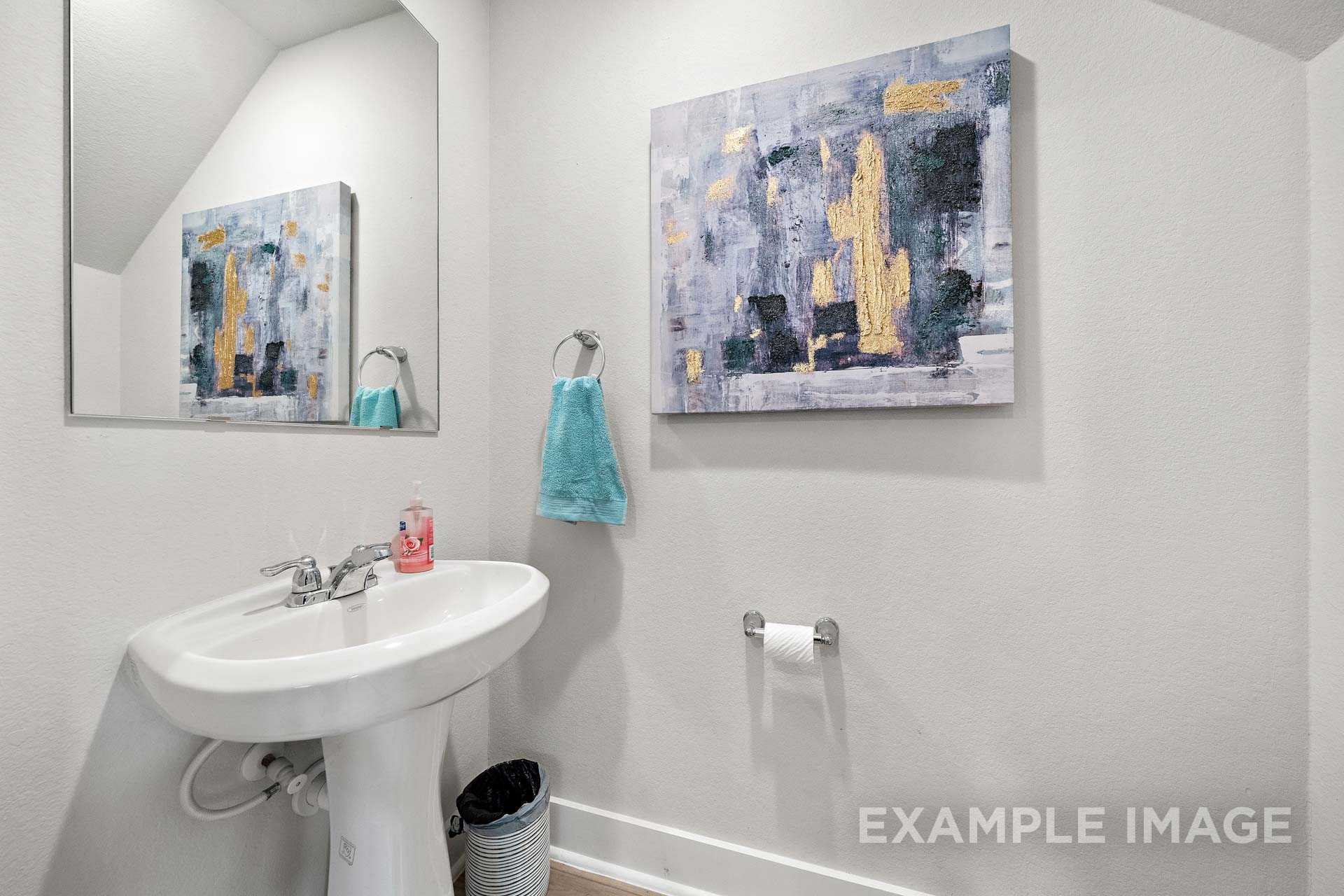 Modern powder room in The Lily A with white pedestal sink, large mirror, abstract gold artwork, and blue towel