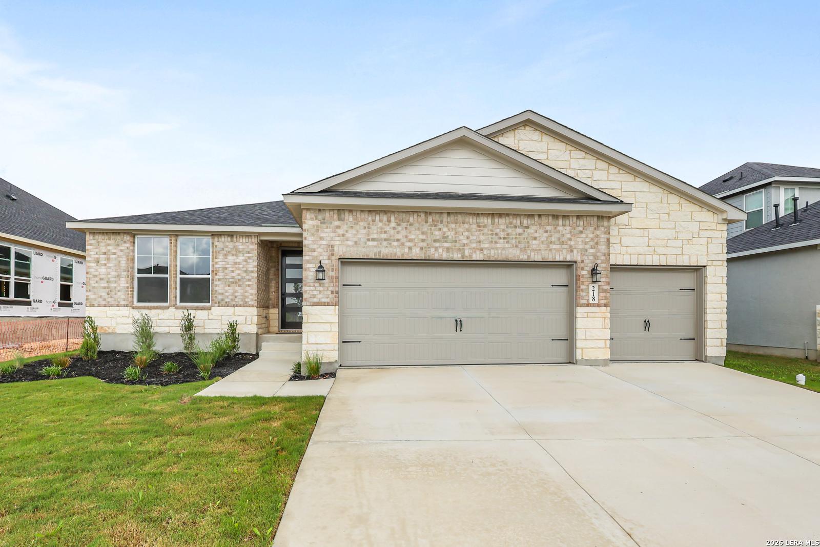 Modern brick and stone single-story home with 2-car garage, driveway, and landscaped yard in The Reserve at Potranco Oaks, Castroville, Texas