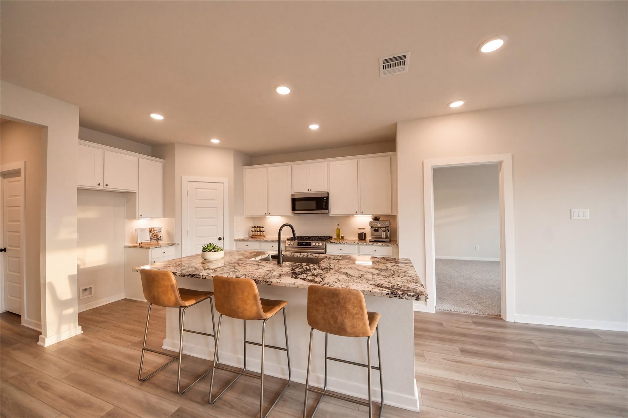 Modern kitchen with granite island, white cabinets, and bar seating in The Everett C floor plan at River Ranch Meadows.