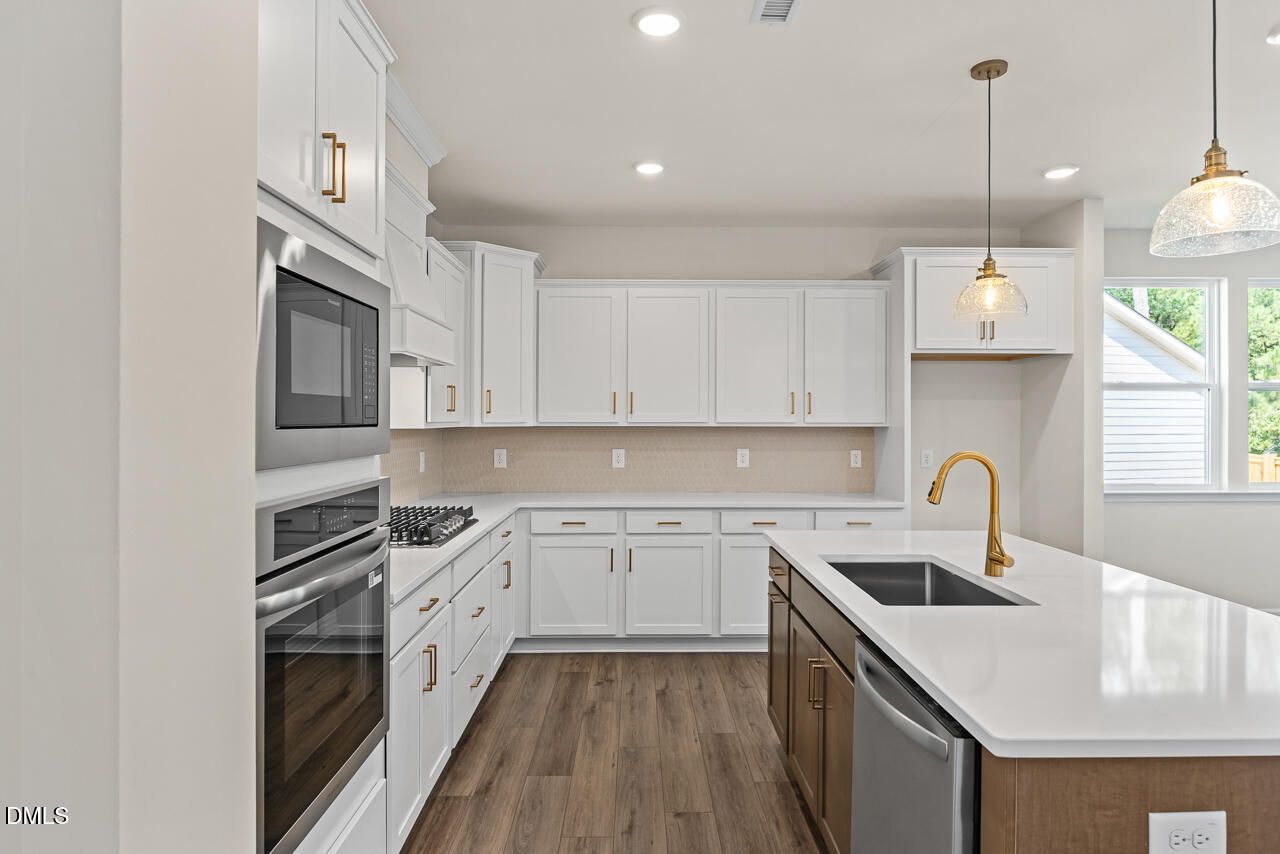 Modern kitchen with white shaker cabinets, gold hardware, island sink, and stainless appliances in Davidson Homes Birch II C, Wake Forest NC