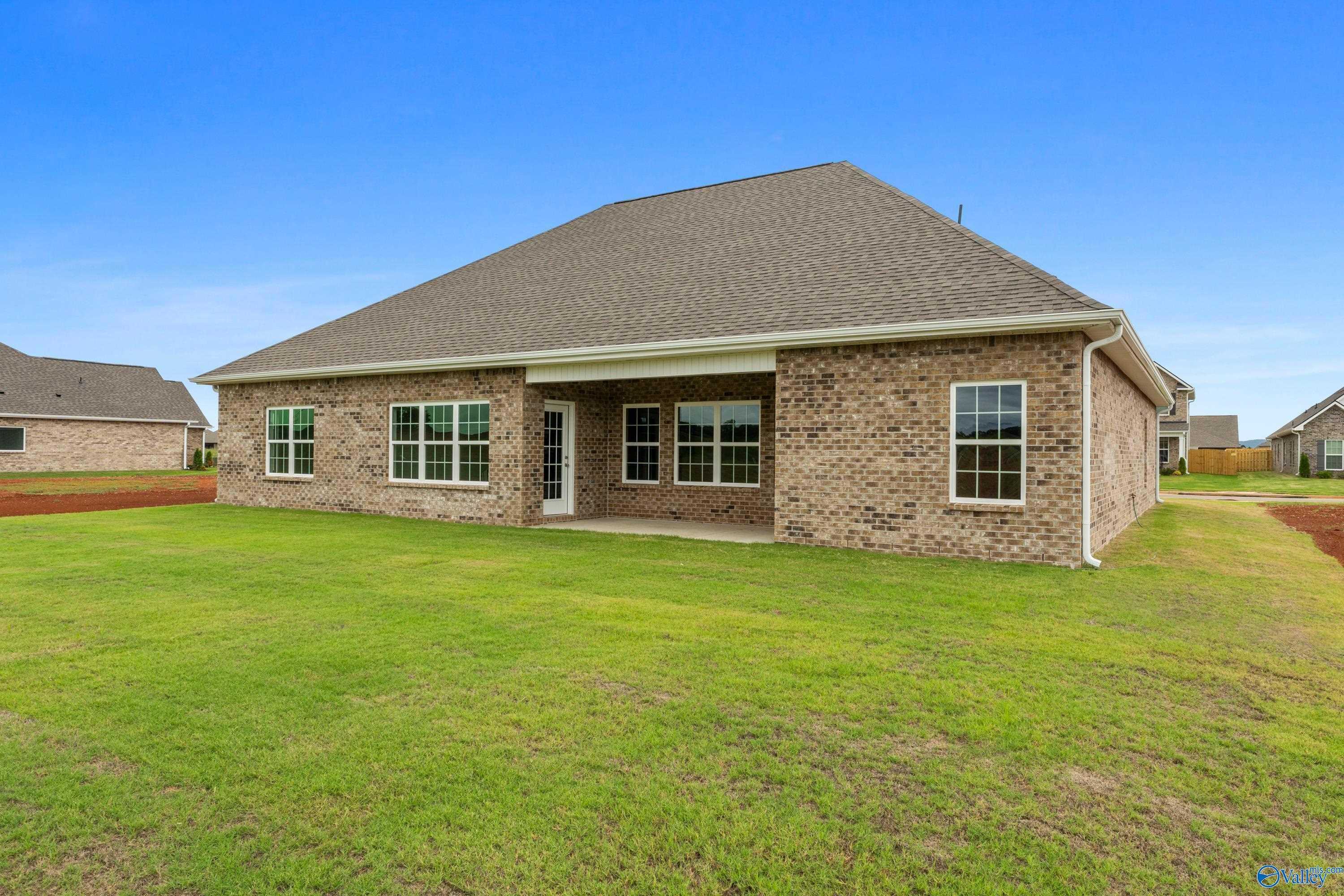 Rear view of The Finleigh 1-story brick home with covered patio, large windows, and lush green lawn in Briercreek, Meridianville, Alabama