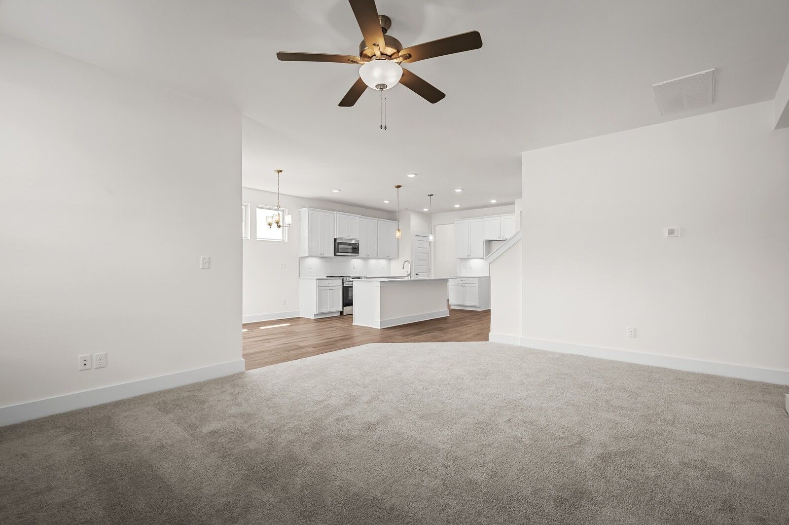 Open-concept living room with ceiling fan leading to modern kitchen in The Ash A floor plan, Woods Crossing, Gallatin, TN.