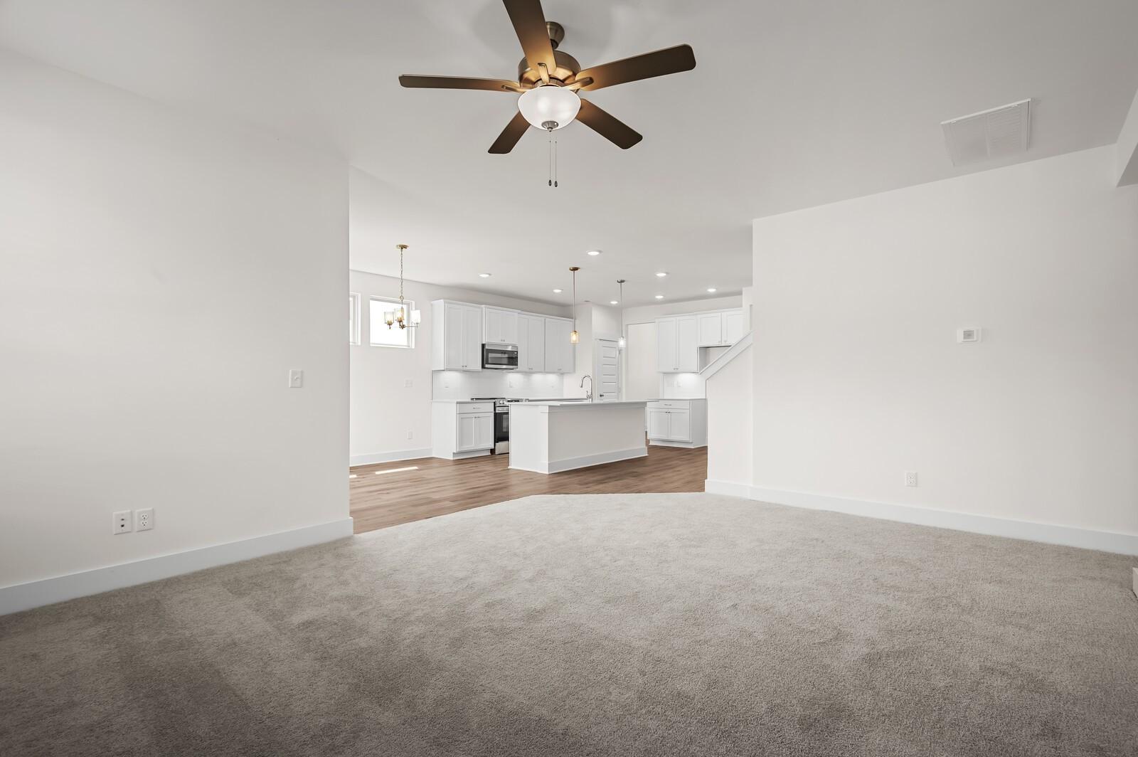Open-concept living room with ceiling fan leading to modern kitchen in The Ash A floor plan, Woods Crossing, Gallatin, TN.