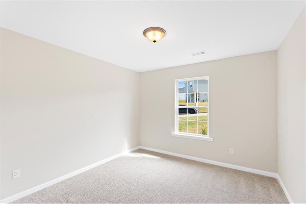 Bright secondary bedroom with beige walls, carpet floor, large window overlooking yard in Davidson Homes The Washington, Phenix City