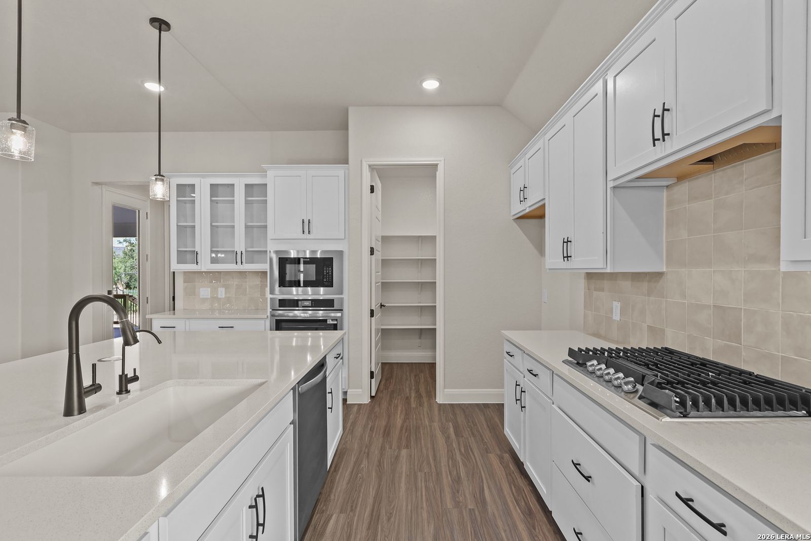 Modern kitchen with white cabinets, quartz countertops, and walk-in pantry in Summerlin B home, Potranco Oaks, Castroville.