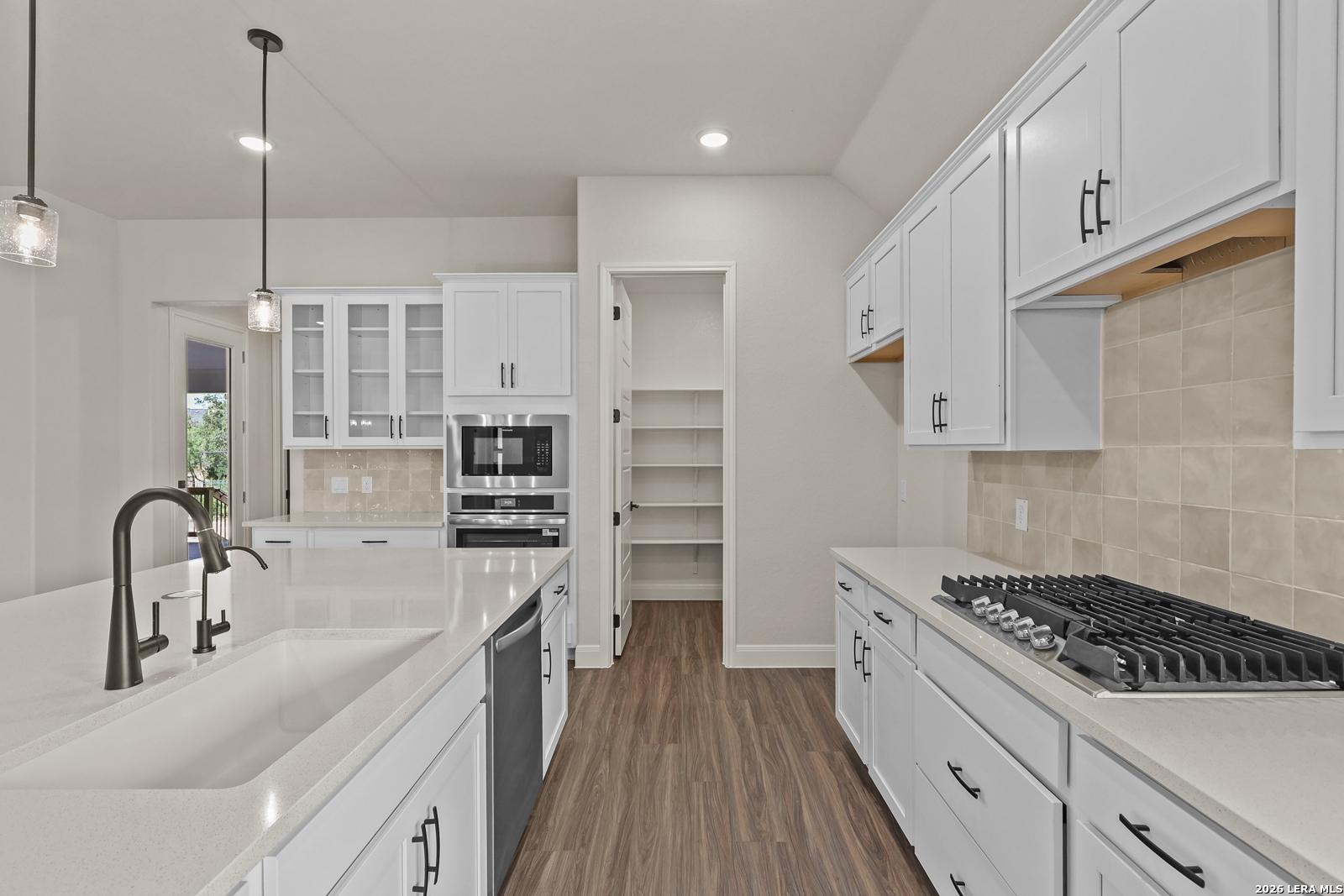 Modern kitchen with white cabinets, quartz countertops, and walk-in pantry in Summerlin B home, Potranco Oaks, Castroville.