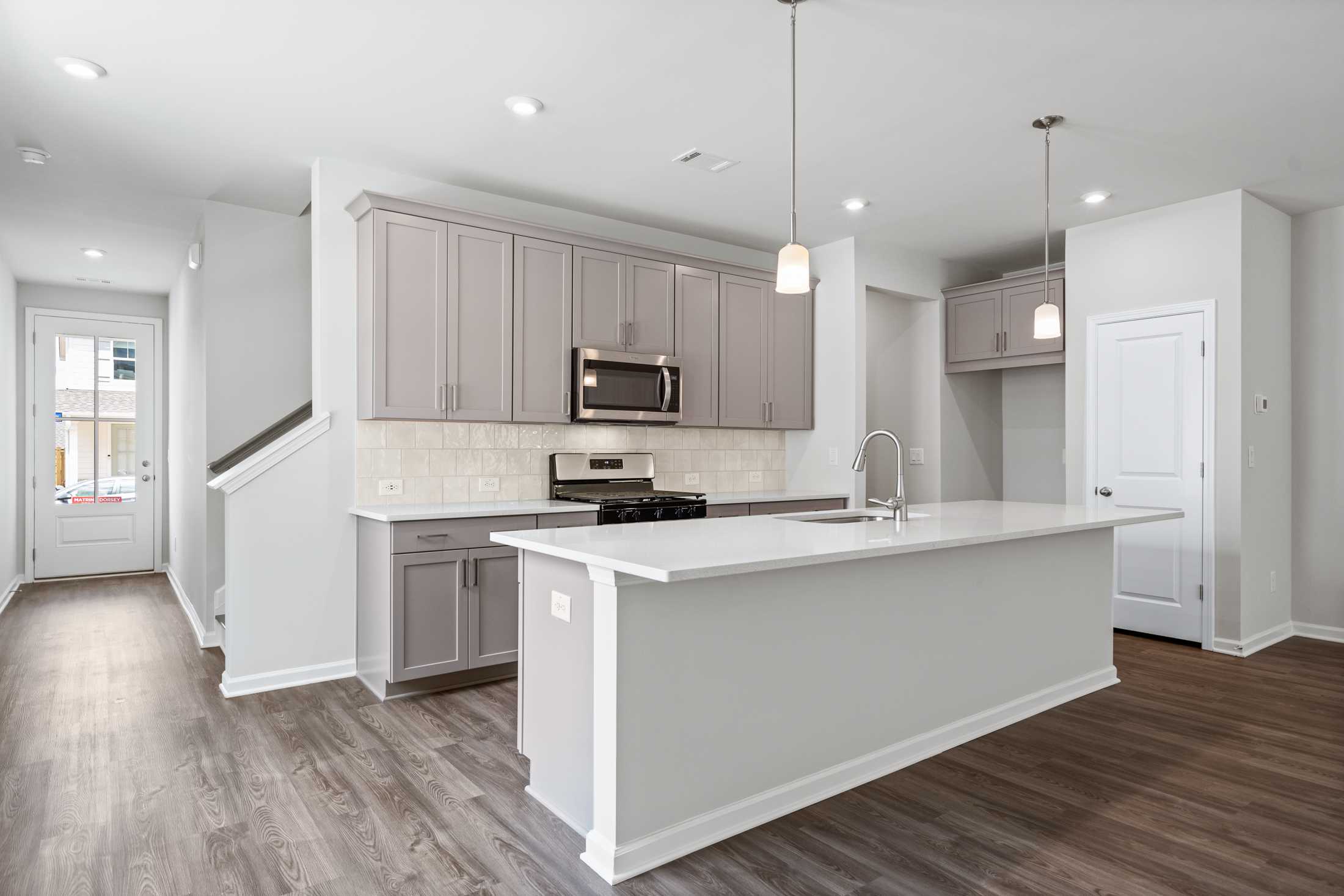 Spacious modern kitchen in The Cary A Davidson Homes design featuring gray shaker cabinets, white quartz island, stainless appliances
