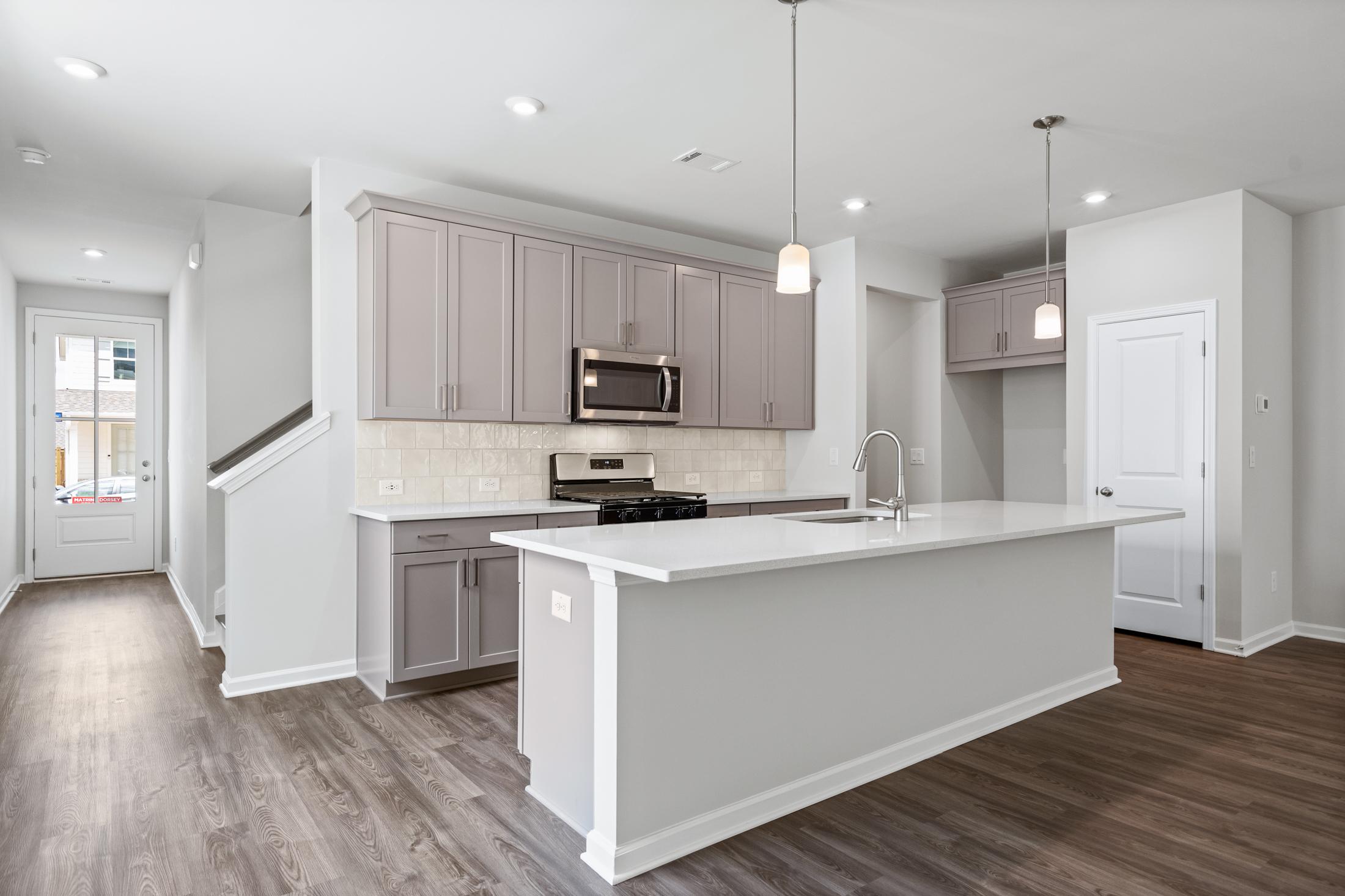 Spacious modern kitchen in The Cary A Davidson Homes design featuring gray shaker cabinets, white quartz island, stainless appliances