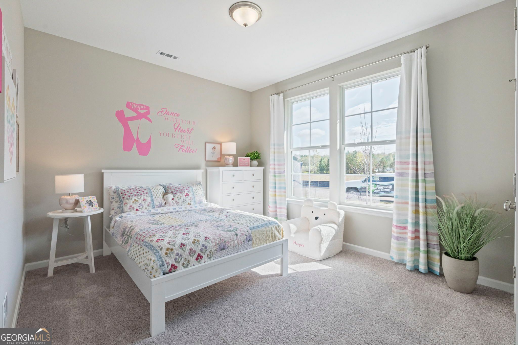 Cozy girl's bedroom with pink ballet wall decal, white bed, patchwork quilt, teddy bear chair, and window in Evermore Homes The Phoenix, Perry, Georgia