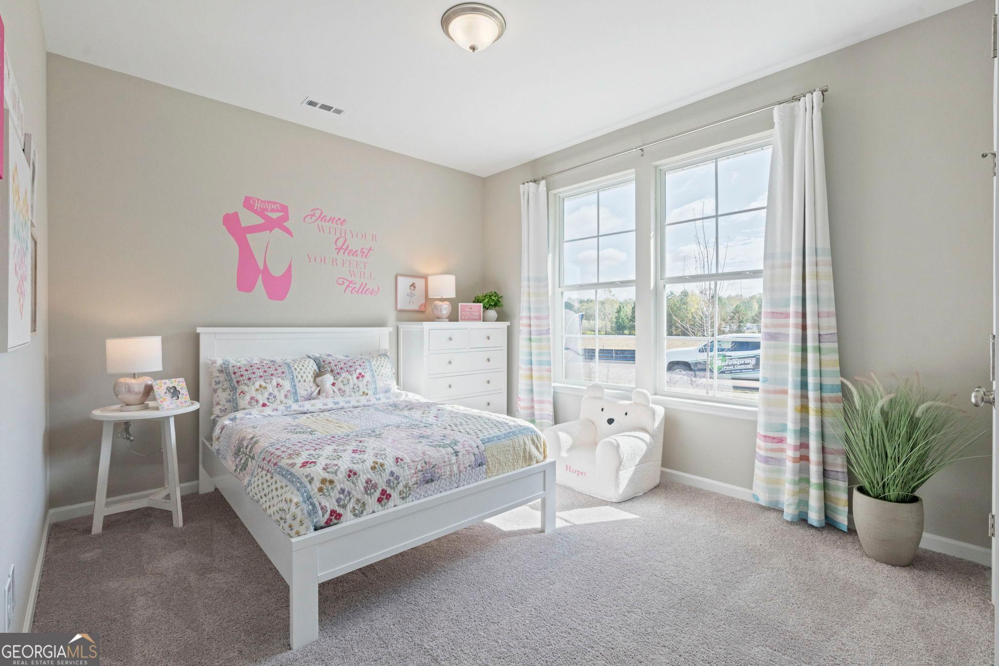 Cozy girl's bedroom featuring ballet-themed wall decal, white bed with colorful quilt, dresser, and large windows in Evermore Homes The Phoenix, Perry, Georgia