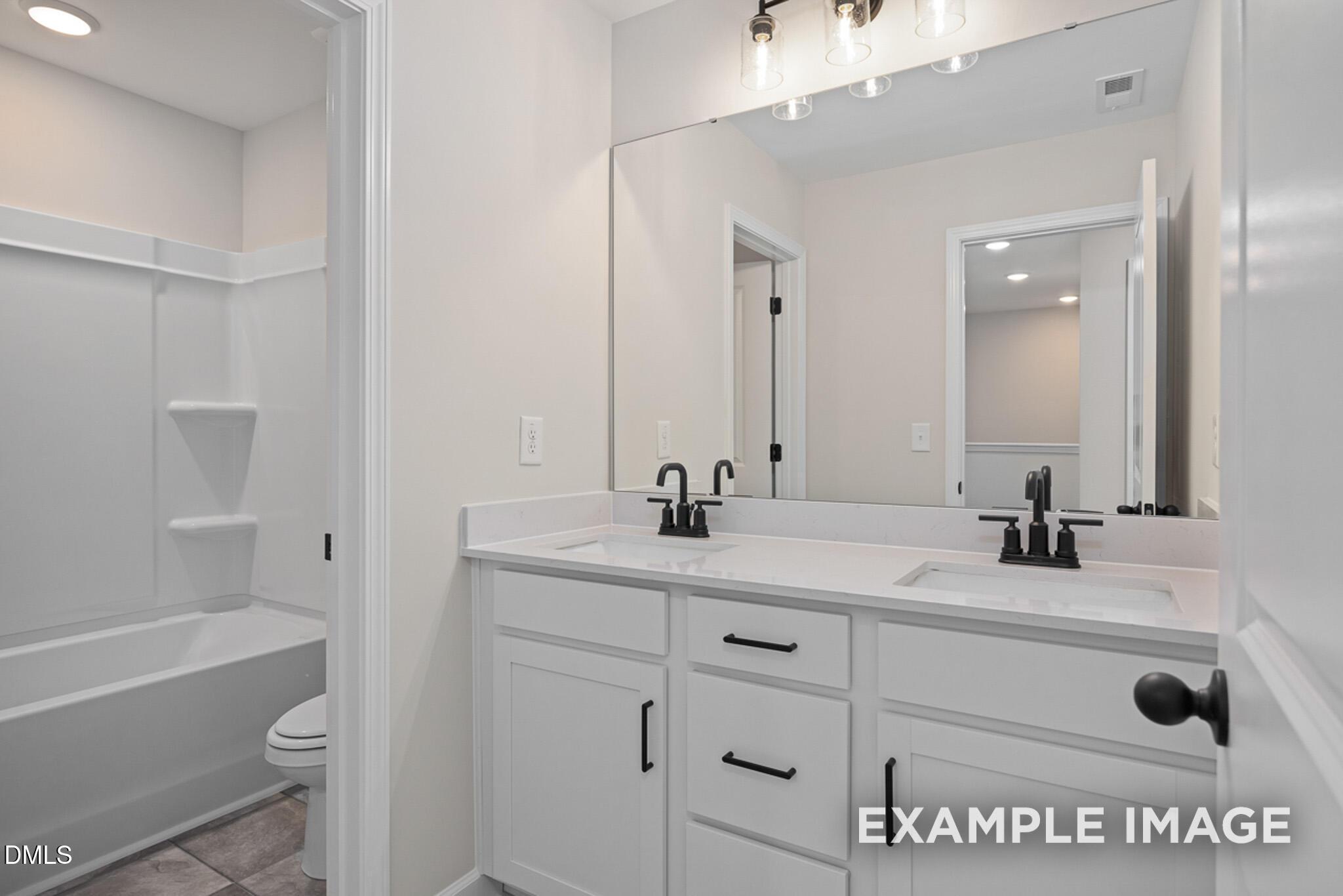 Modern bathroom with double vanity, white cabinets, and tub-shower combo in Mitchell floor plan at Camden Park, Knightdale.