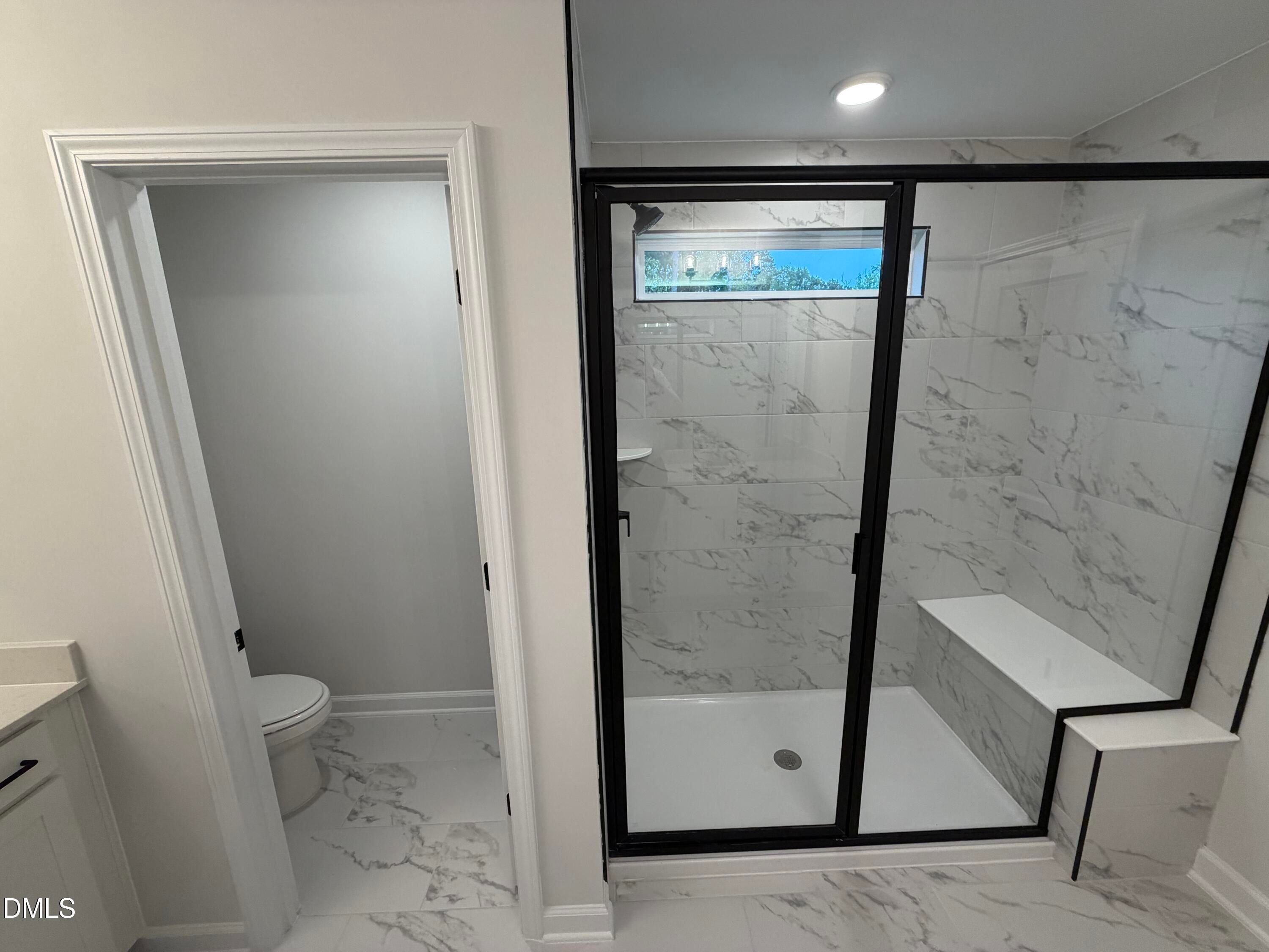 Modern bathroom with marble tile walk-in shower, black-framed glass door, and built-in bench in Davidson Homes' Preston C, Wendell NC