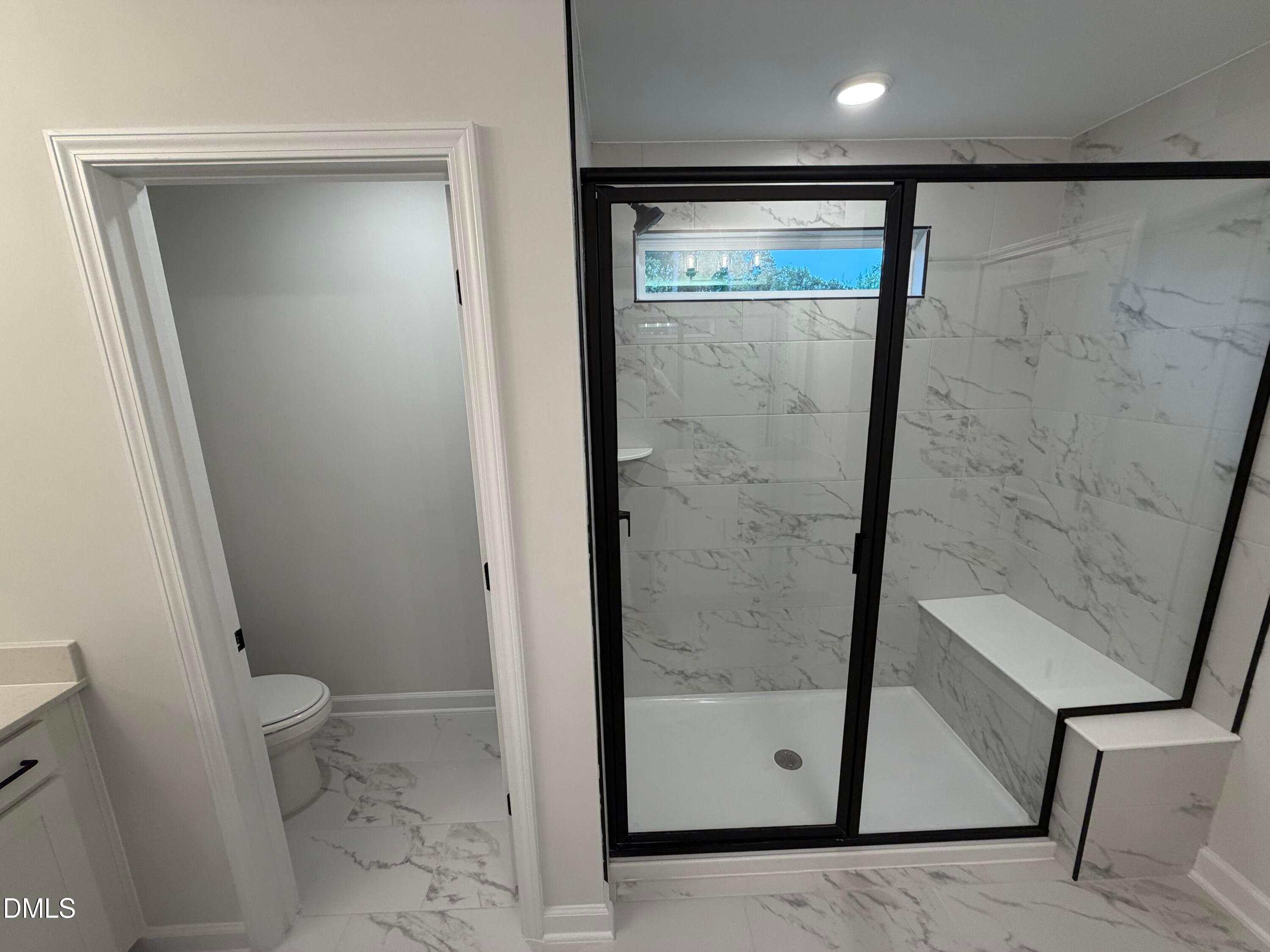 Modern bathroom with marble tile walk-in shower, black-framed glass door, and built-in bench in Davidson Homes' Preston C, Wendell NC